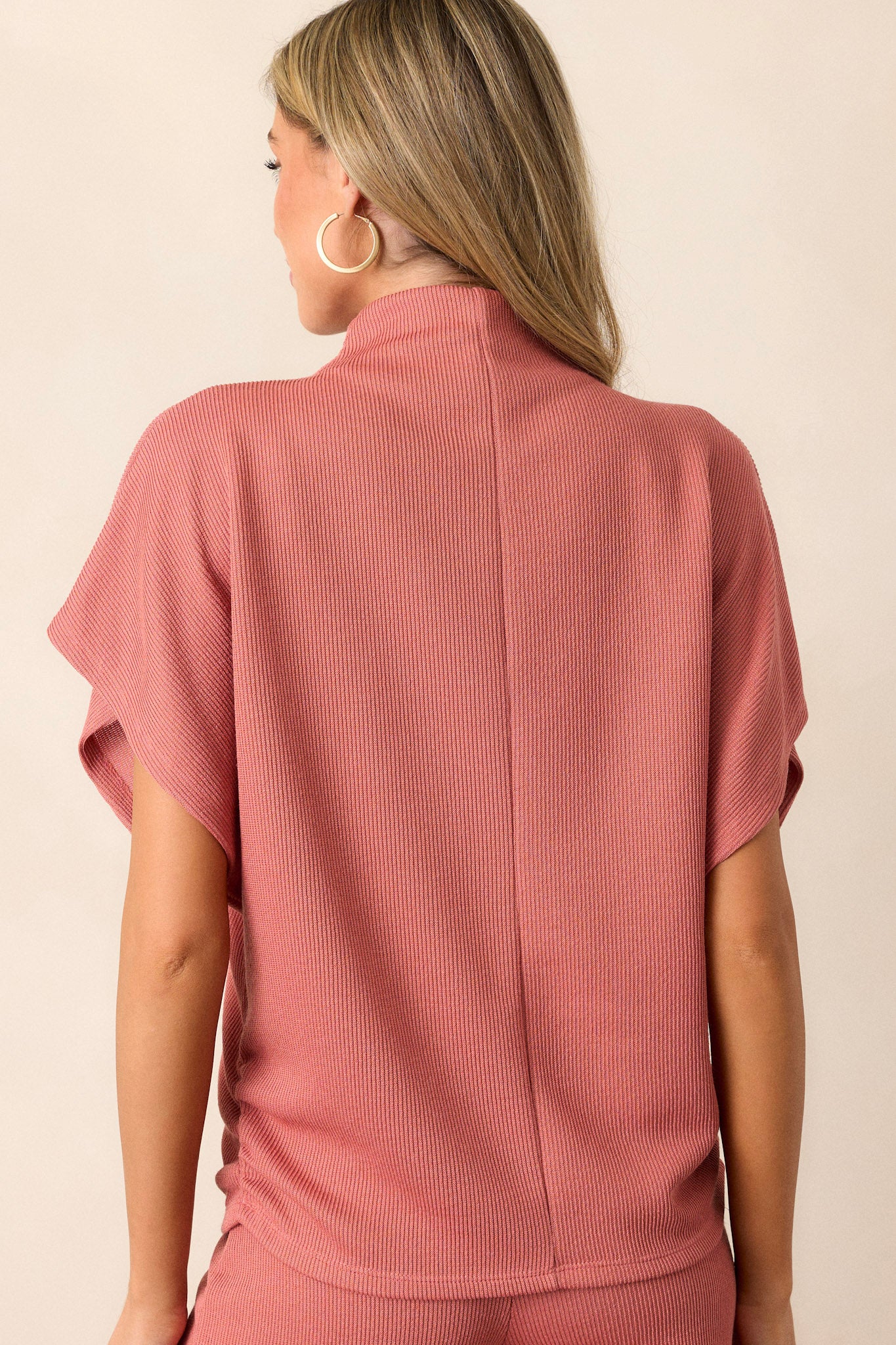 Back view of this coral top that features a turtleneck, a knit towel like texture on the outside, a soft smooth inside, cinching in the hips and short flowy sleeves.