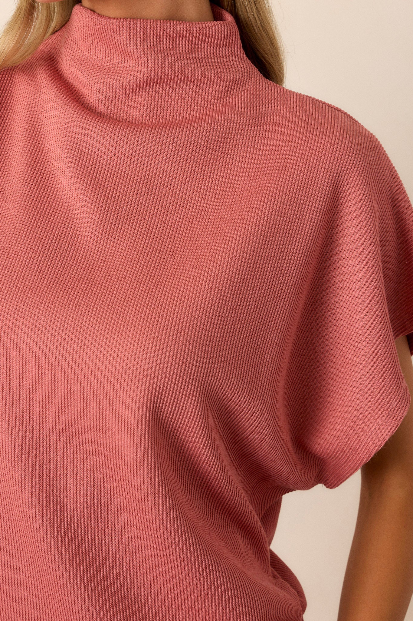 Close-up of this coral top that features a turtleneck, a knit towel like texture on the outside, a soft smooth inside, cinching in the hips and short flowy sleeves.