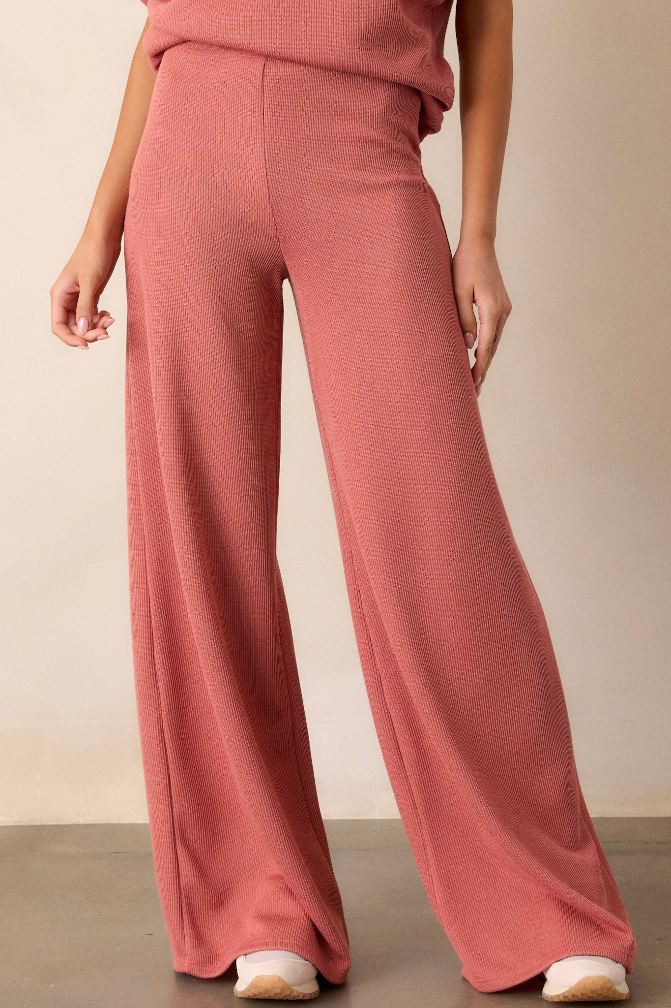 Front angled view of these coral knitted pants that feature an elastic waist band, a high waisted design, a knit towel like texture on the outside, a soft inside and a wide leg.