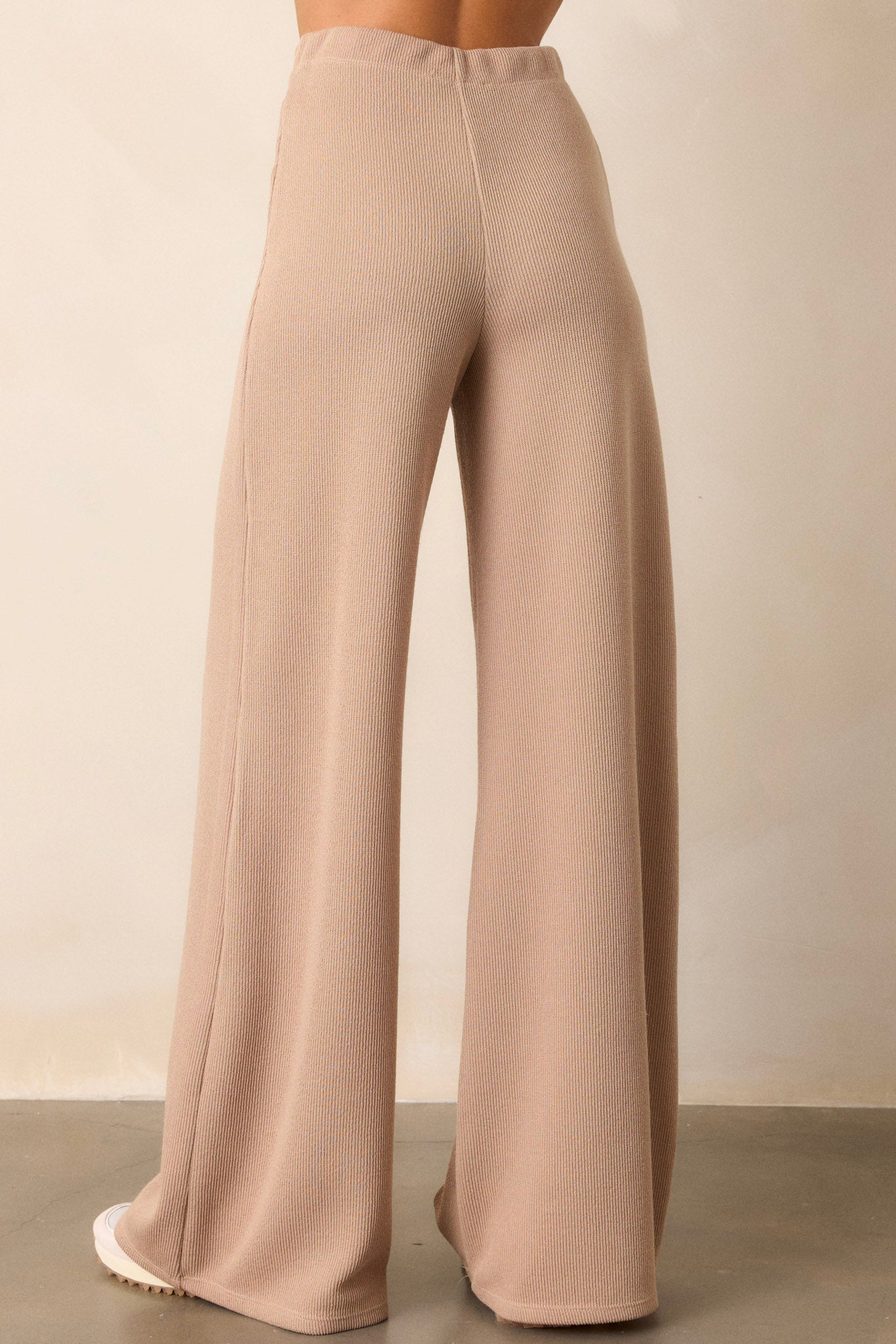 Back view of the beige knitted pants highlighting the wide leg, the soft inside fabric, and the high-waisted design with the elastic waistband.