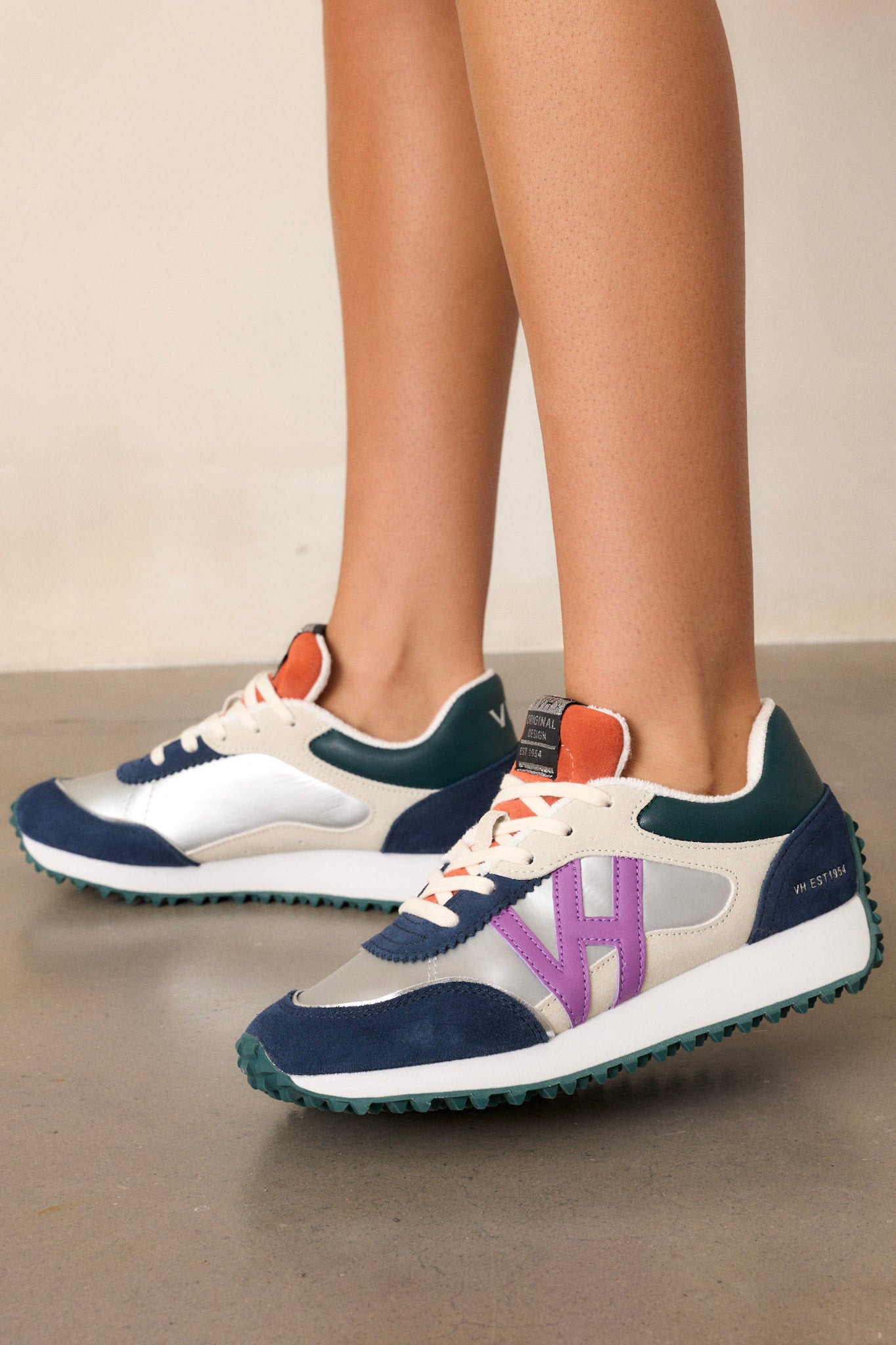 Angled view of these silver sneakers that feature a rounded toe, functional laces, subtle pops of purple, navy, orange and silver, a slight platform, and a heavily textured sole.