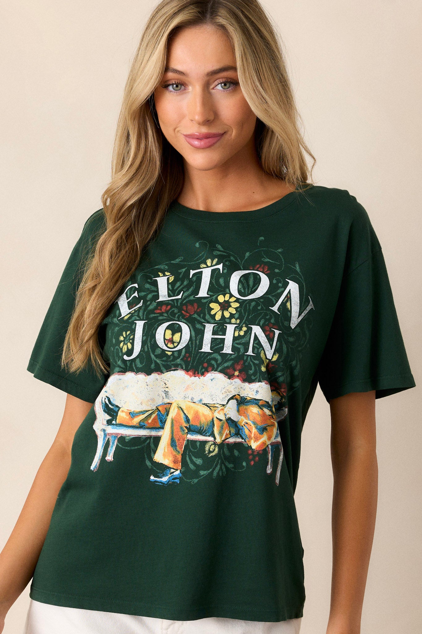 Angled front view of this hunter green tee that features a rounded neckline, a relaxed fit, a portrait of Elton John kicked back amidst floral accents.