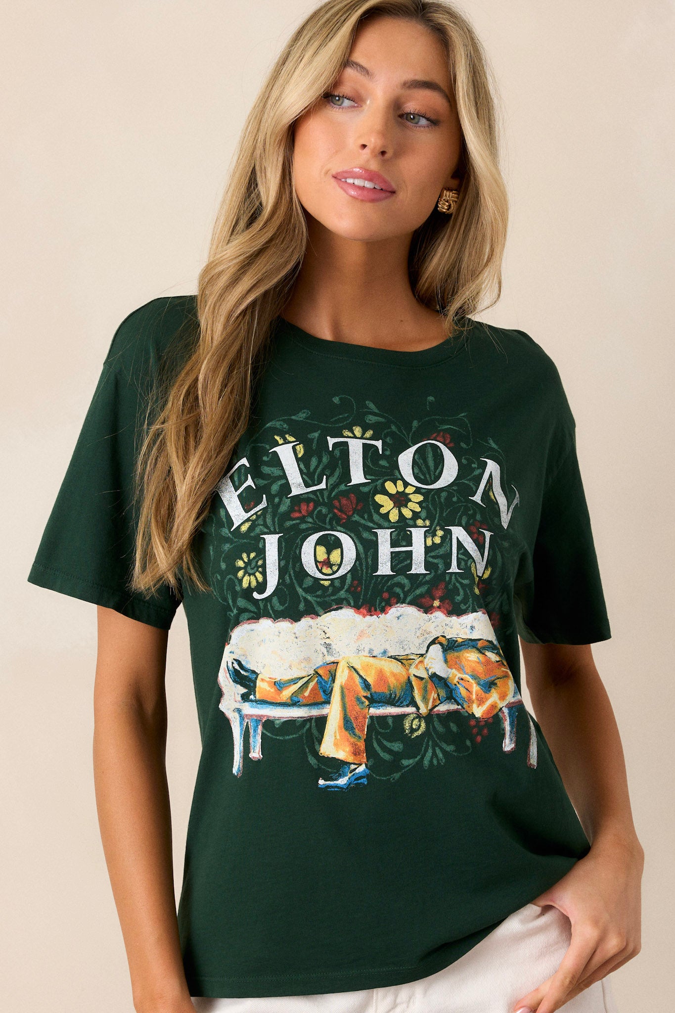 Front view of this hunter green tee that features a rounded neckline, a relaxed fit, a portrait of Elton John kicked back amidst floral accents.