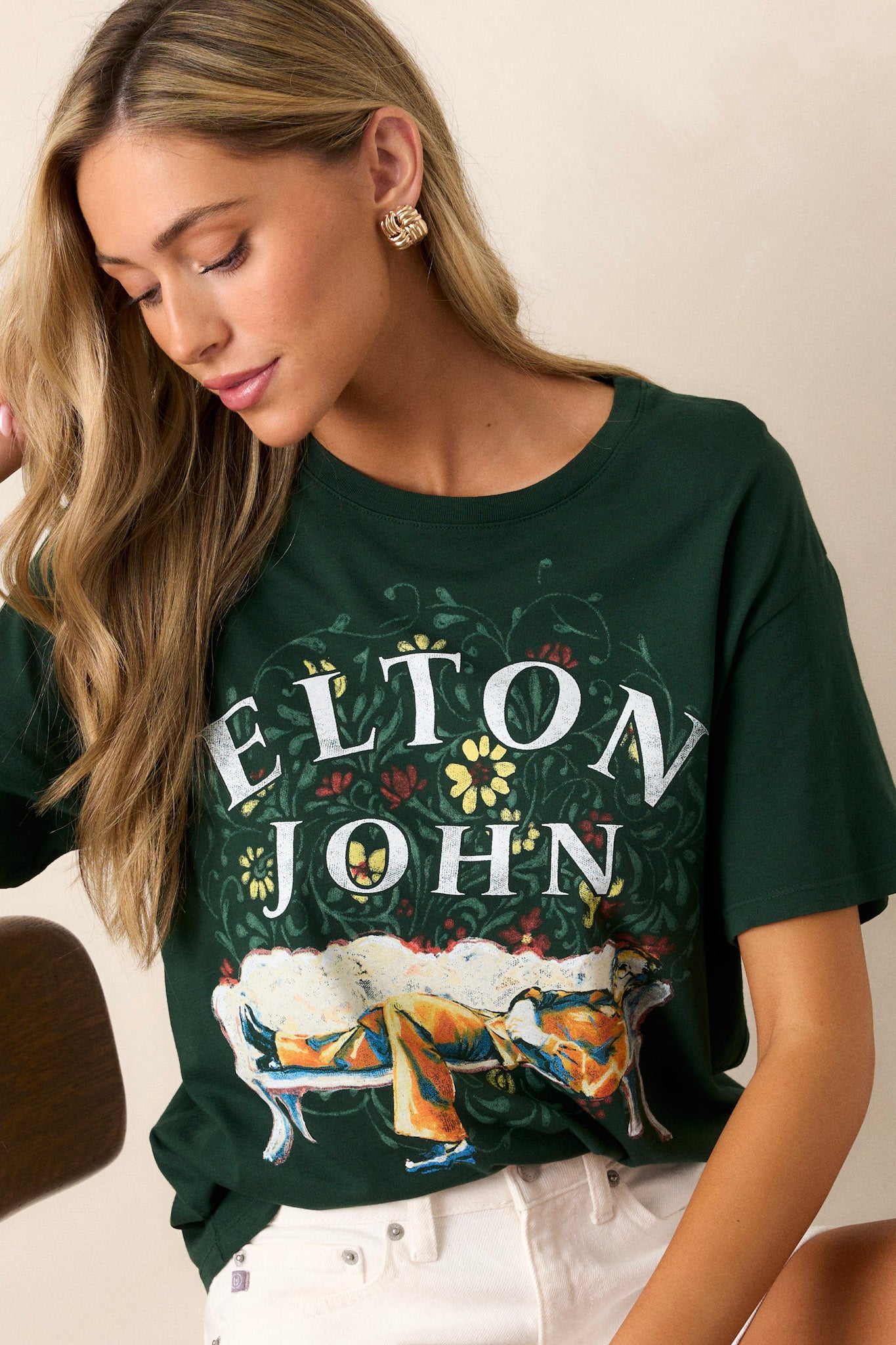 Close-up of this hunter green tee that features a rounded neckline, a relaxed fit, a portrait of Elton John kicked back amidst floral accents.