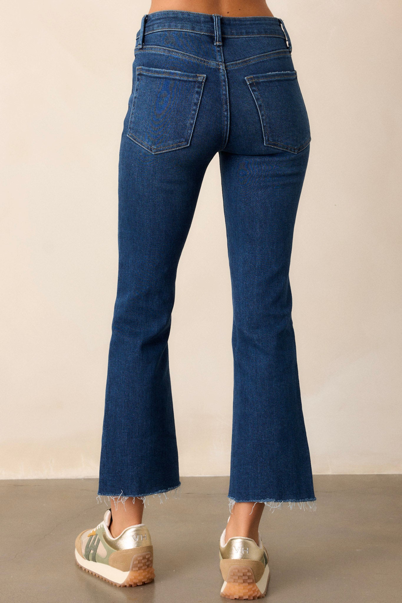 Back view of dark wash jeans with functional belt loops, functional back pockets, a flare design, and a cropped hem.