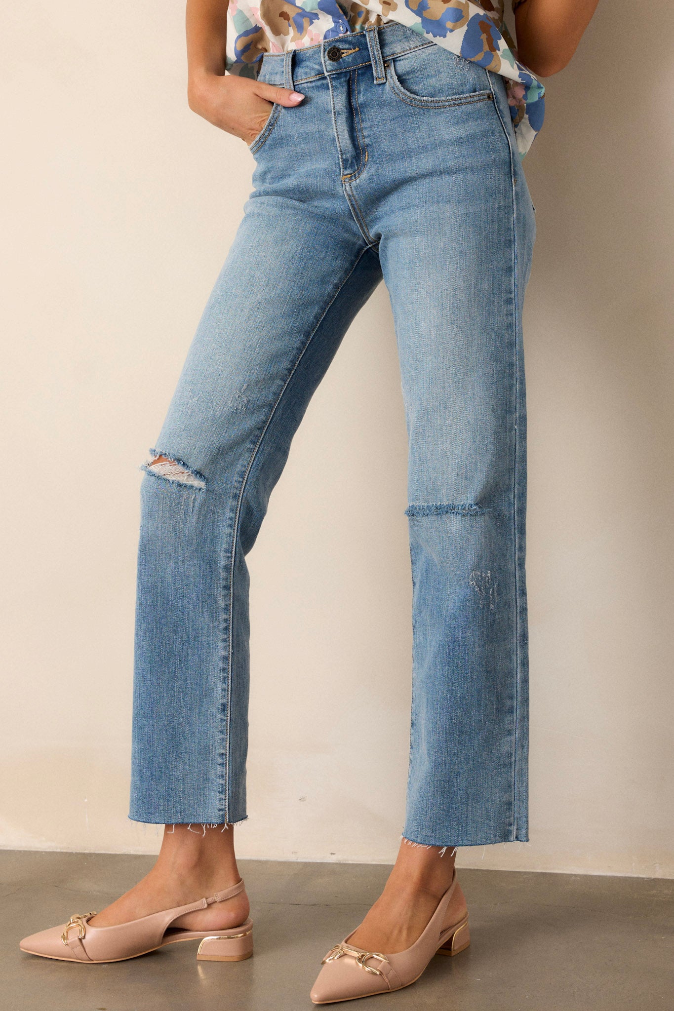 Front angled view of jeans featuring a high waisted design, button and zipper closure, belt loops, functional front and back pockets, distressing, and a raw hemline