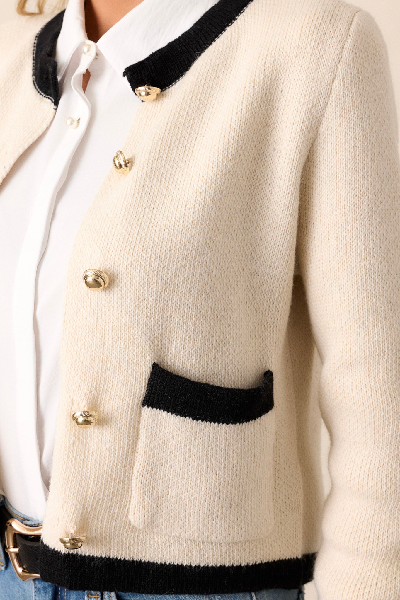 Close up of the small functional and black trimmed pockets and the gold buttons on this ivory, black trimmed cardigan.