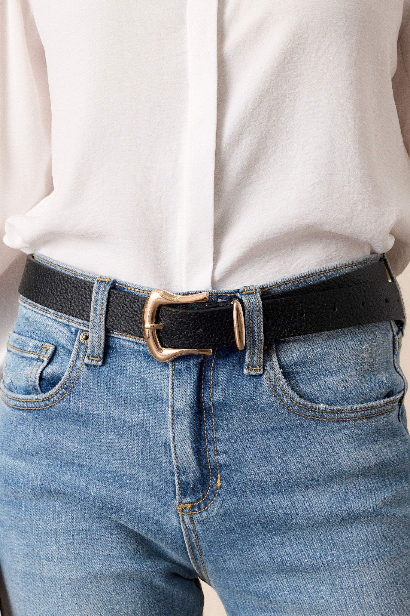 This black belt features gold hardware, a horseshoe pin buckle, and a textured faux leather material.