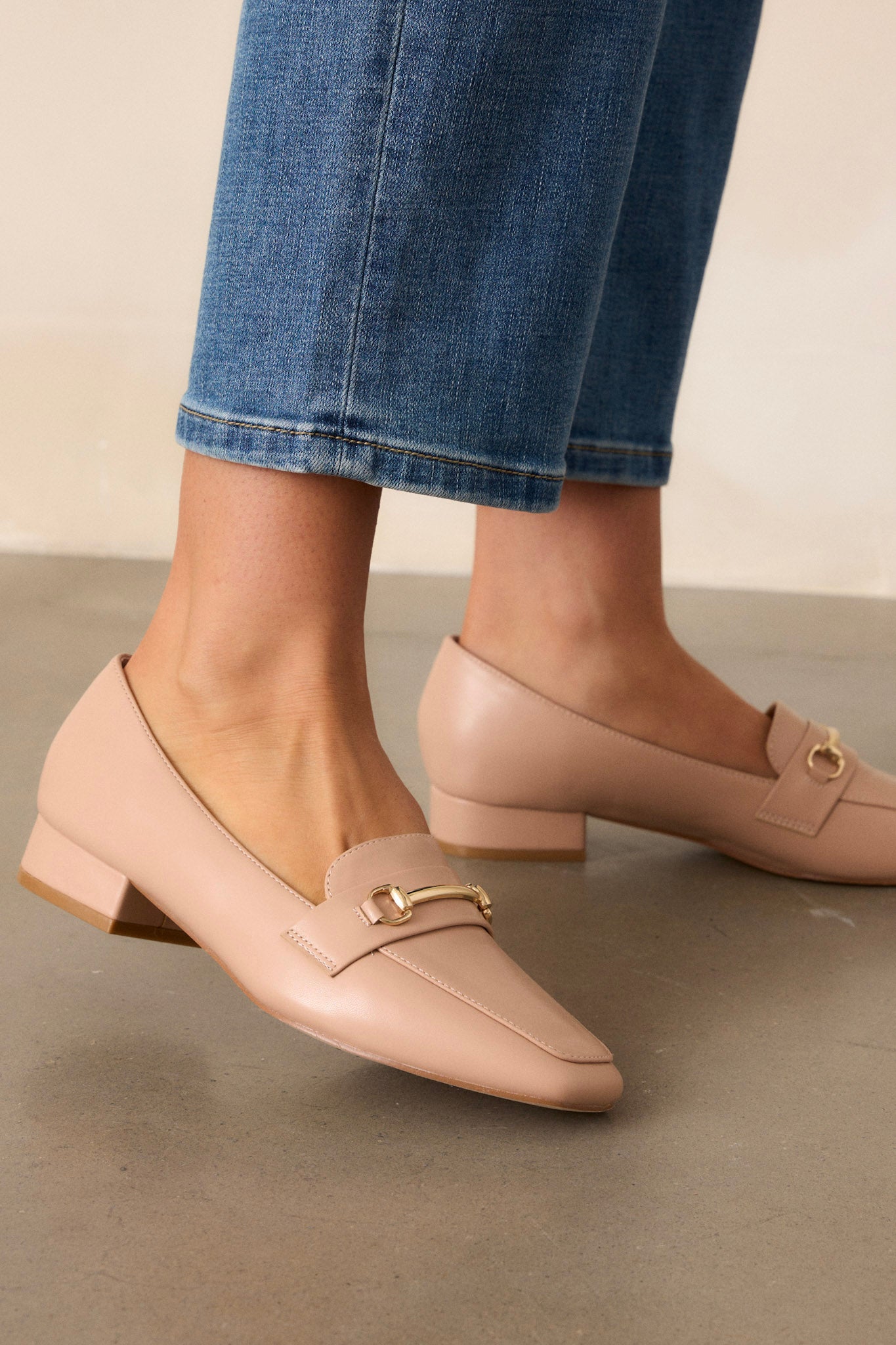 Close up view of these beige loafers that feature a slip on design, a small heel, a square toe, and gold hardware