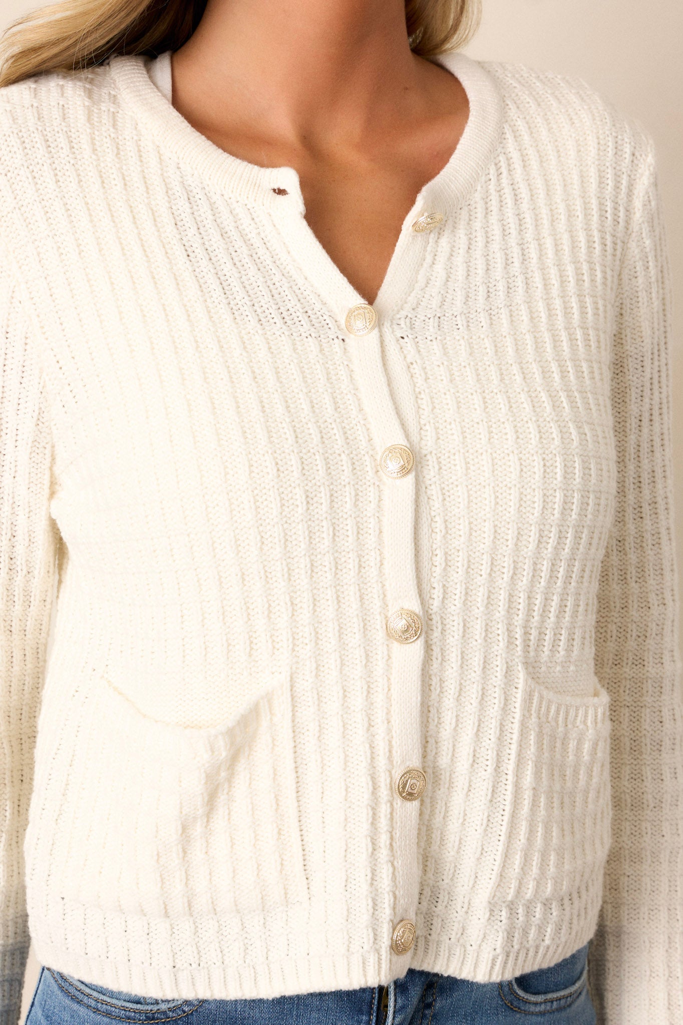 Close-up of the ivory sweater focusing on the gold hardware and the ribbed texture, along with a clear view of the front functional pockets.