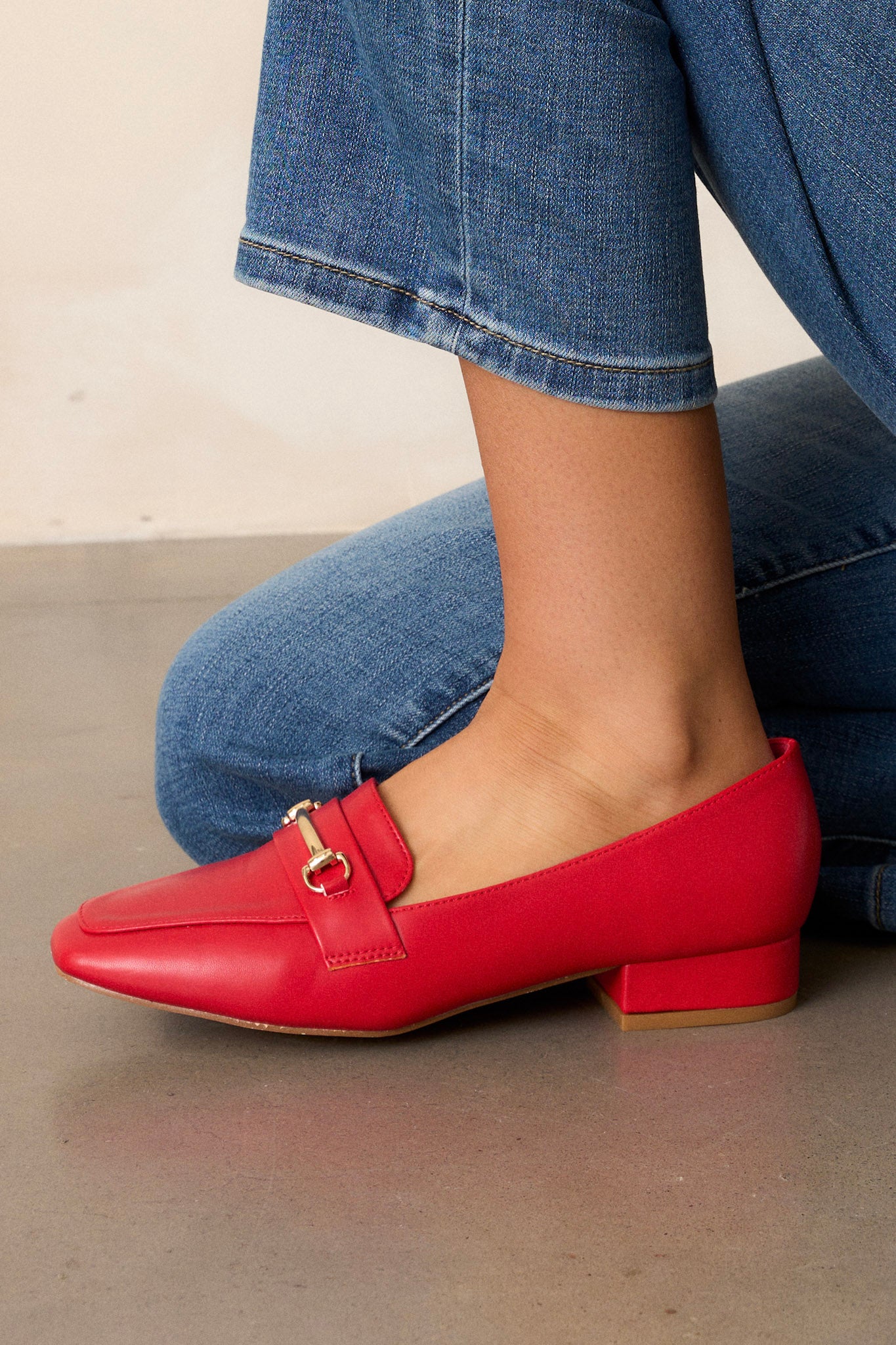 Close up view of these red loafers that feature a slip on design, a small heel, a square toe, and gold hardware.