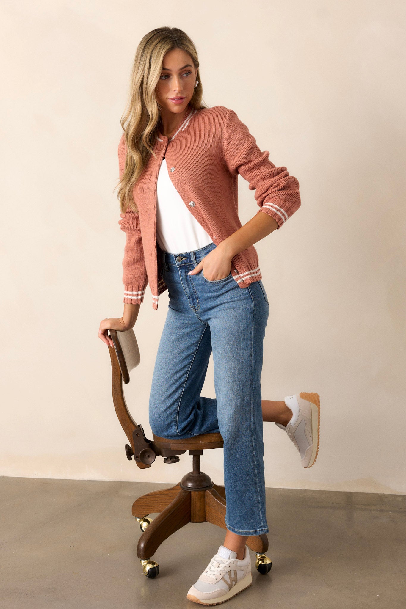 Side view of this terracotta knit cardigan that features a rounded neckline, a functional button front, a white stripe trim on the neckline, cuffs of the sleeves & the hemline, a soft knit texture and long sleeves.