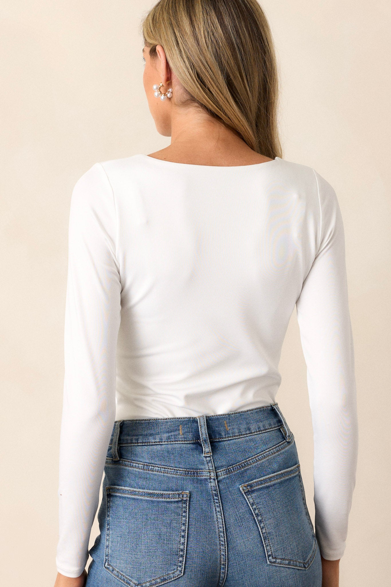 Back view of this ivory bodysuit that features a square neckline, long sleeves, and bottom snap button closures.