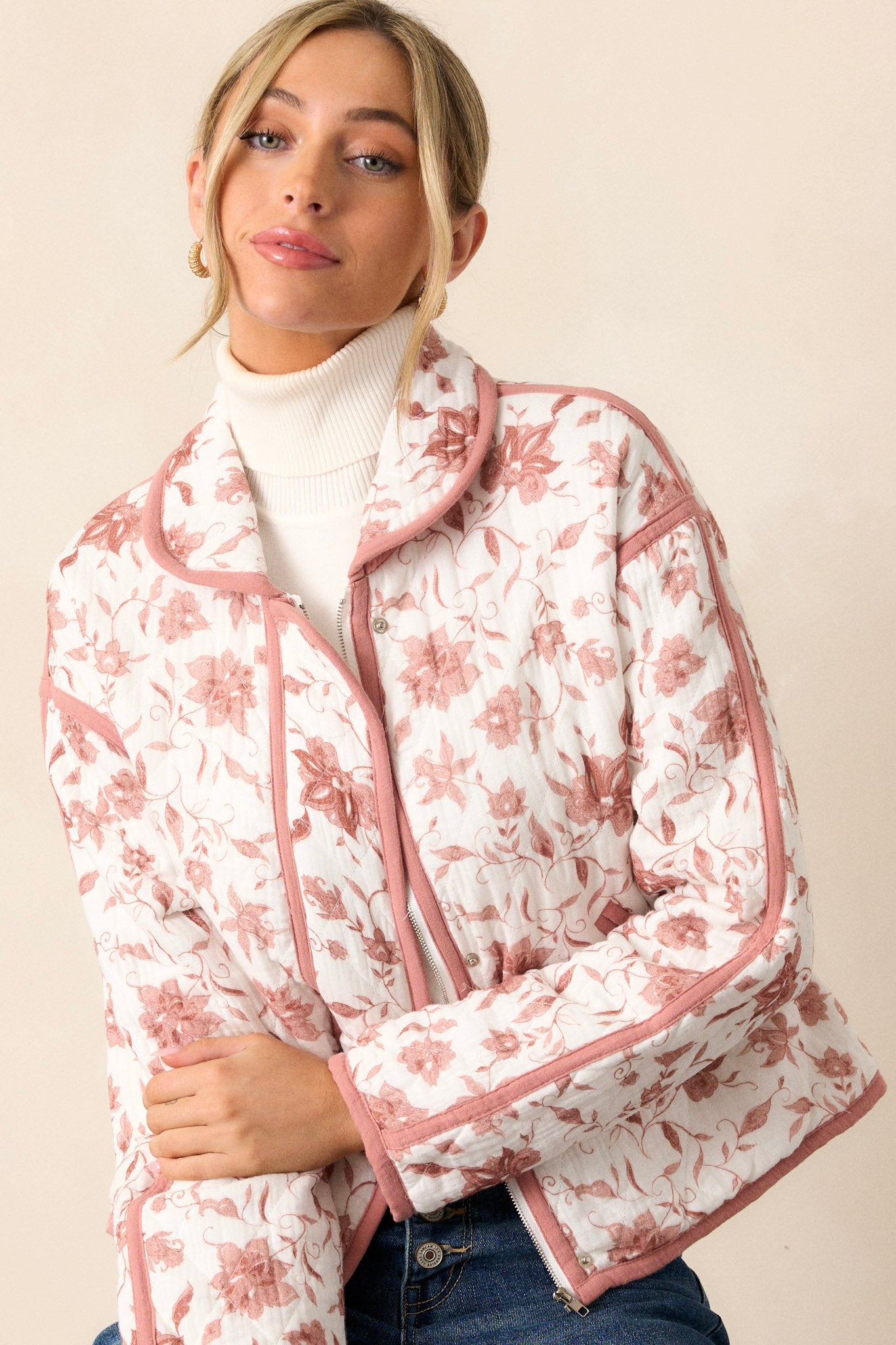 This dusty pink jacket features a collared neckline, a full zip front, a solid dusty pink trim, an ivory floral print, a soft quilted material and snap buttons for extra support.