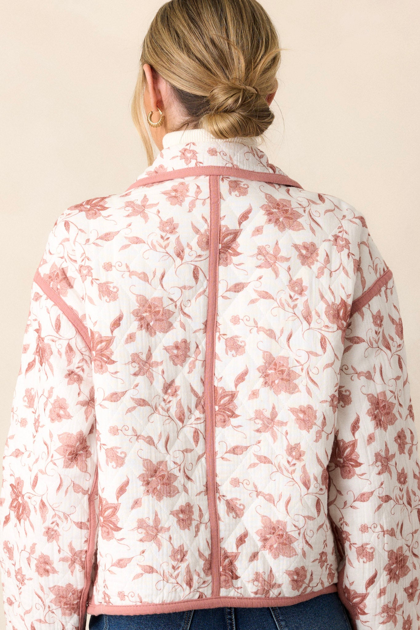 Back view of this dusty pink jacket that features a collared neckline, a full zip front, a solid dusty pink trim, an ivory floral print, a soft quilted material and snap buttons for extra support.