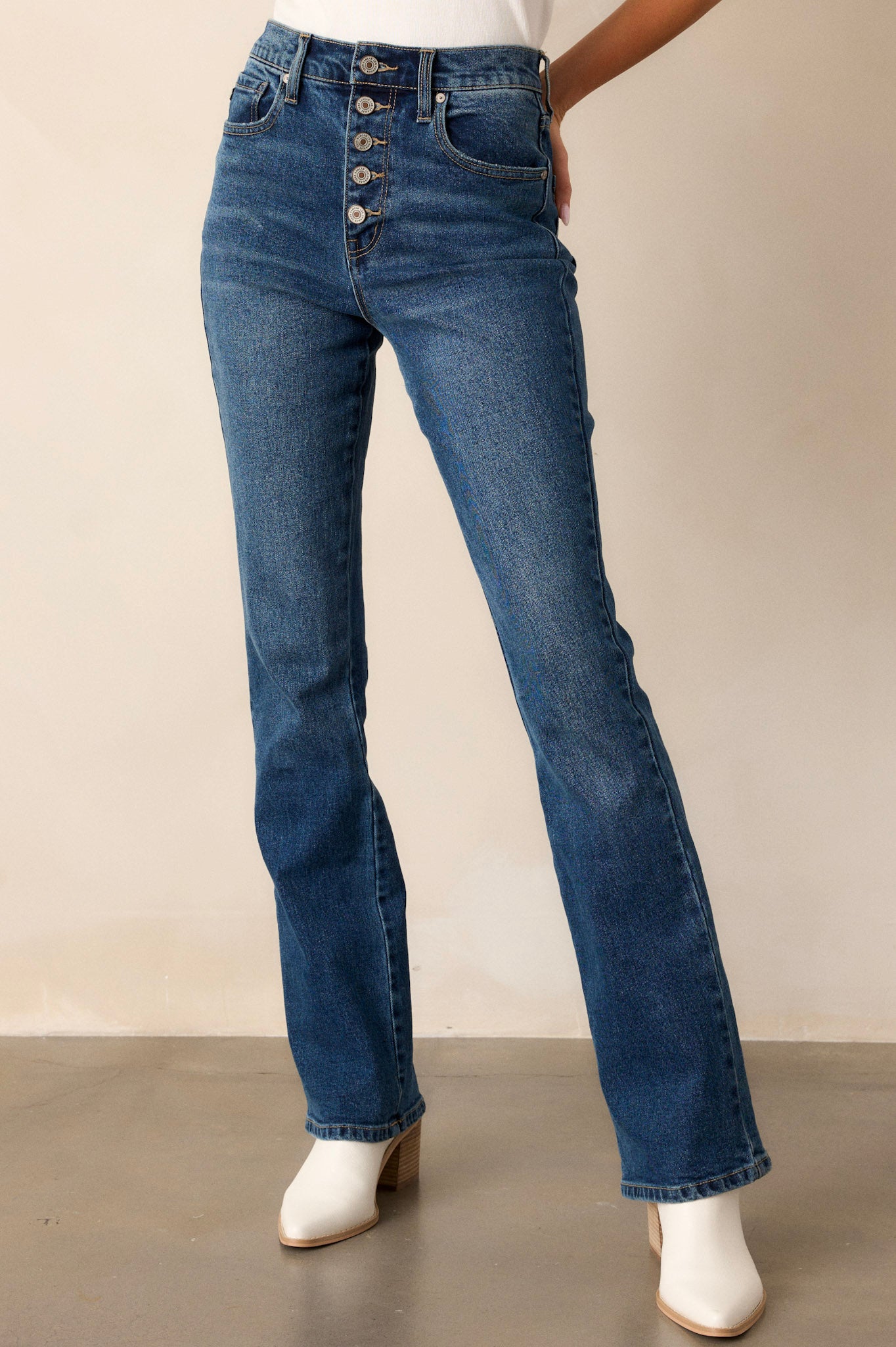 Angled view of these dark wash jeans featuring a high waist with a butterfly button detail, functional belt loops and pockets, and a straight leg style.