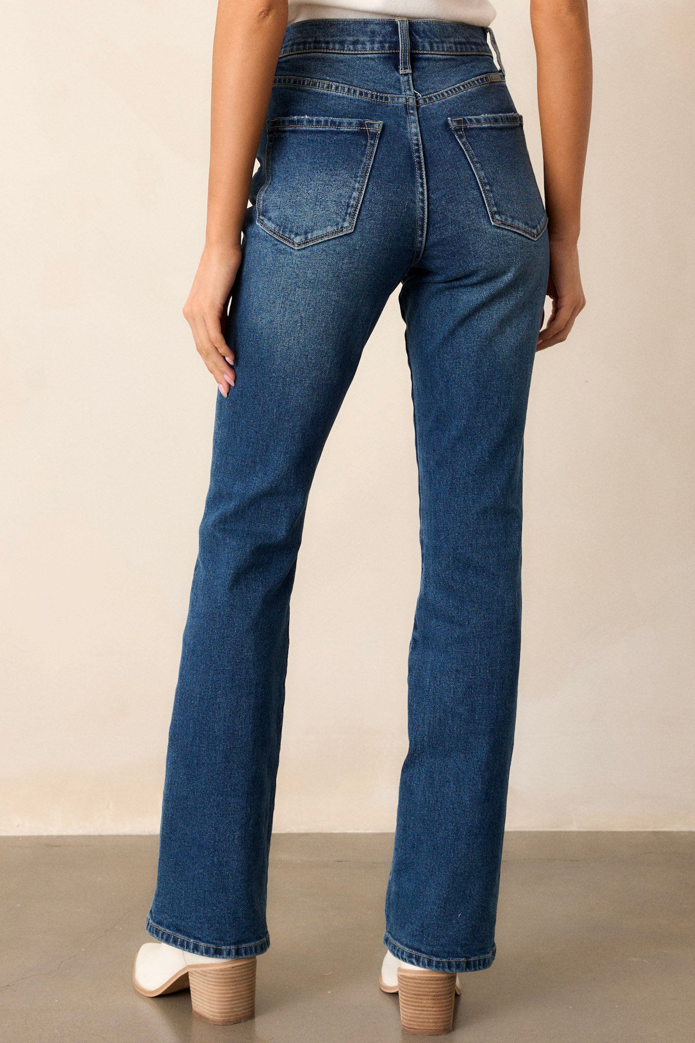 Back view of these dark wash jeans featuring a high waist with a butterfly button detail, functional belt loops and pockets, and a straight leg style.