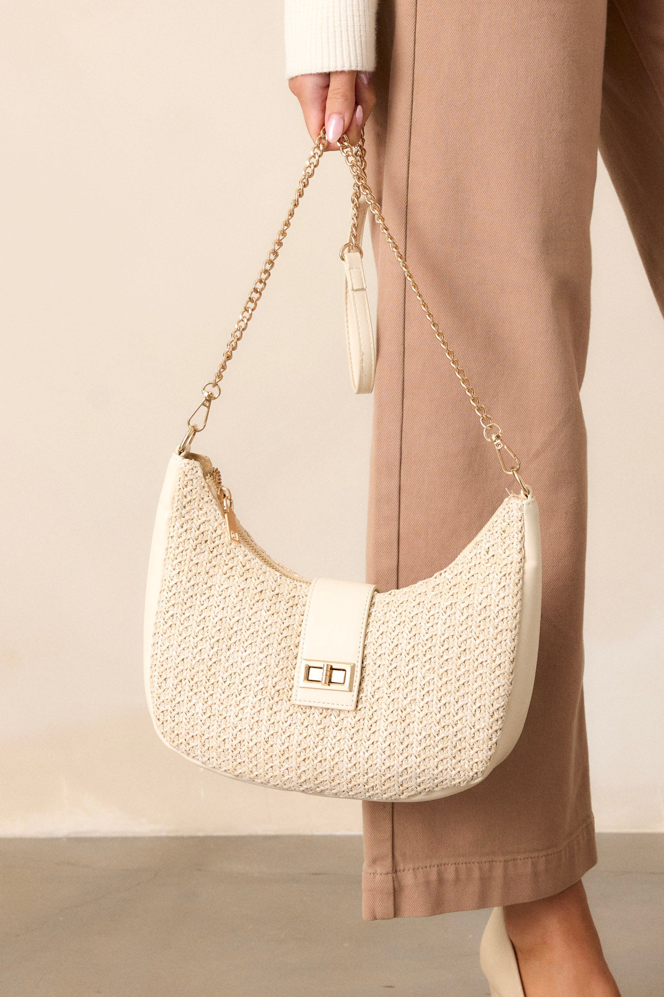 This ivory bag features an ivory shoulder strap, an optional crossbody chain strap, a top flap closure with a turn lock fastening, gold hardware, and a woven texture.