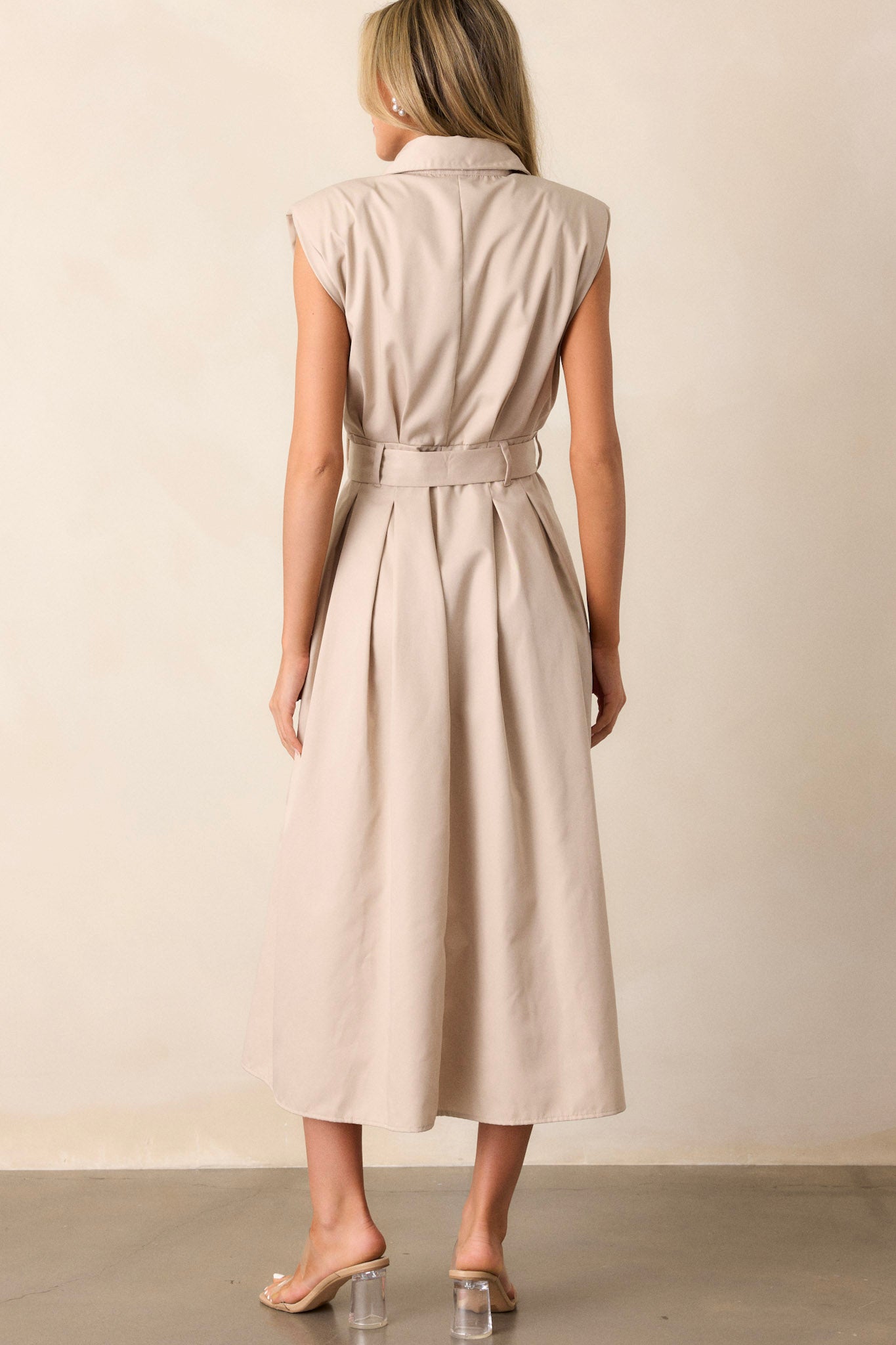 Back view of this beige dress that features built-in shoulder pads, a functional belt and a functional button front.