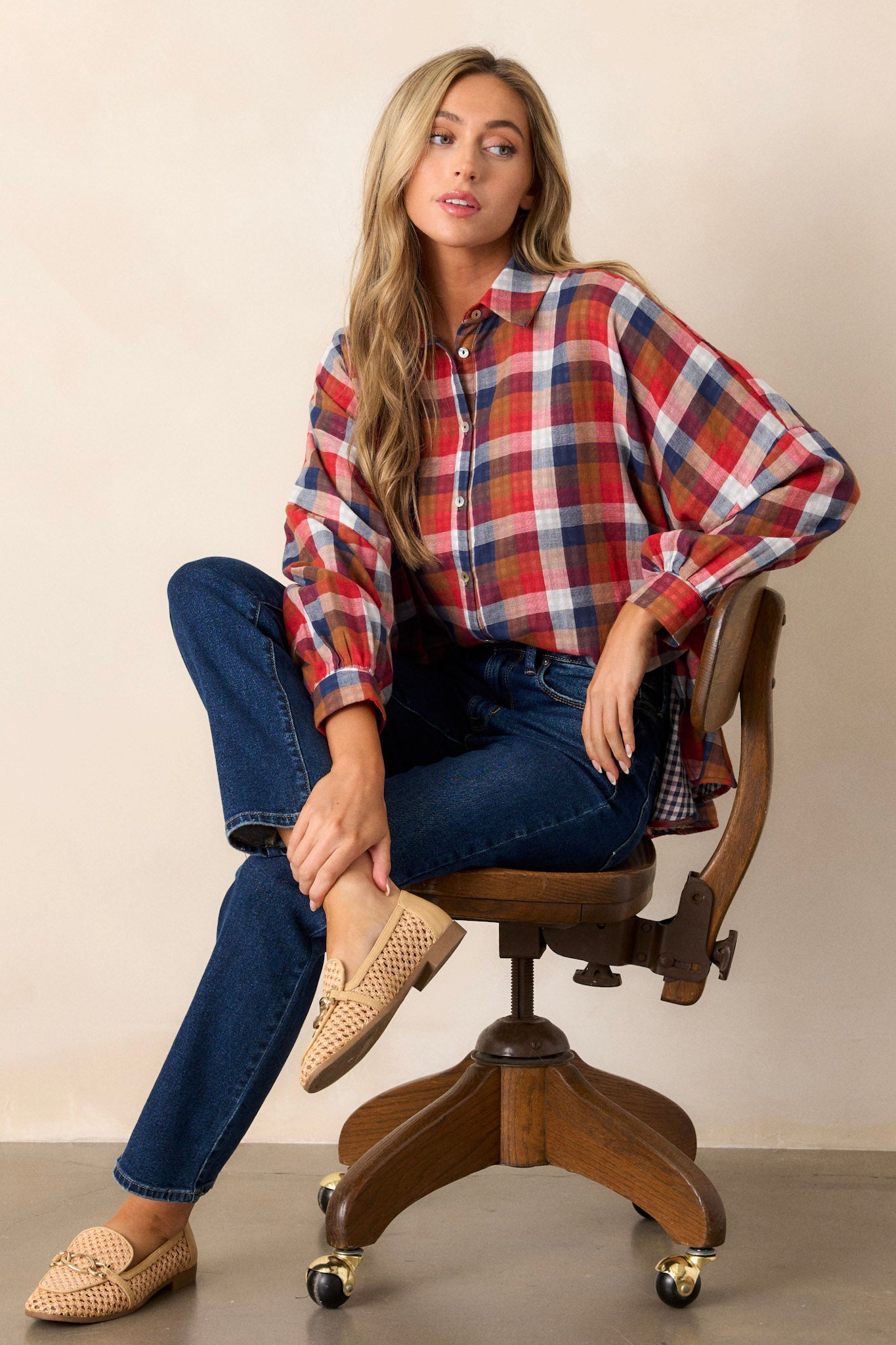 Seated view of a top featuring a collared neckline, functional buttons down the front, cuffed sleeves, a different print on the interior, and an oversized fit