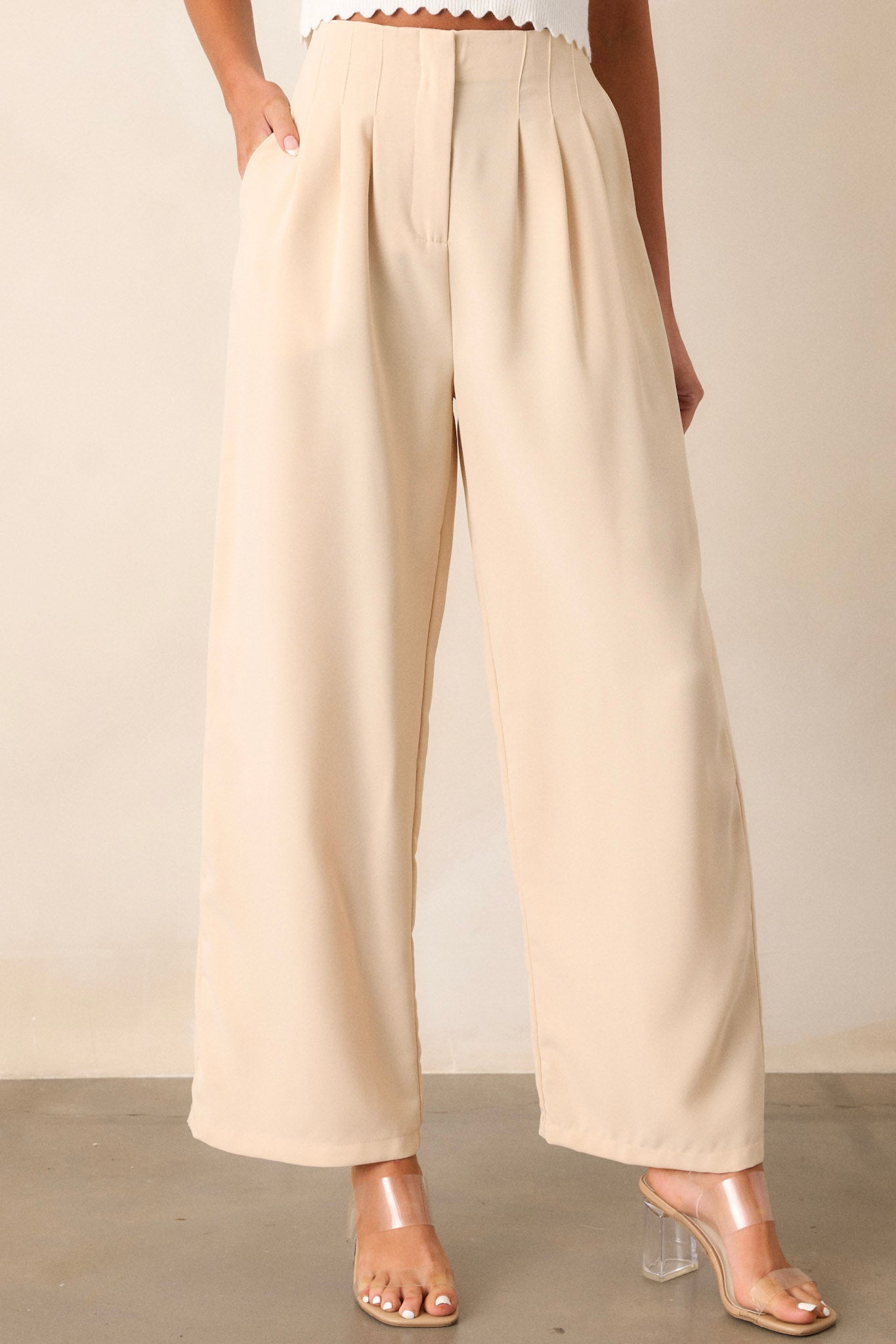 Angled view of the beige pants displaying the fitted waistband, slight pleats, functional hip pockets, and the wide leg design, with a focus on the high-waisted fit.