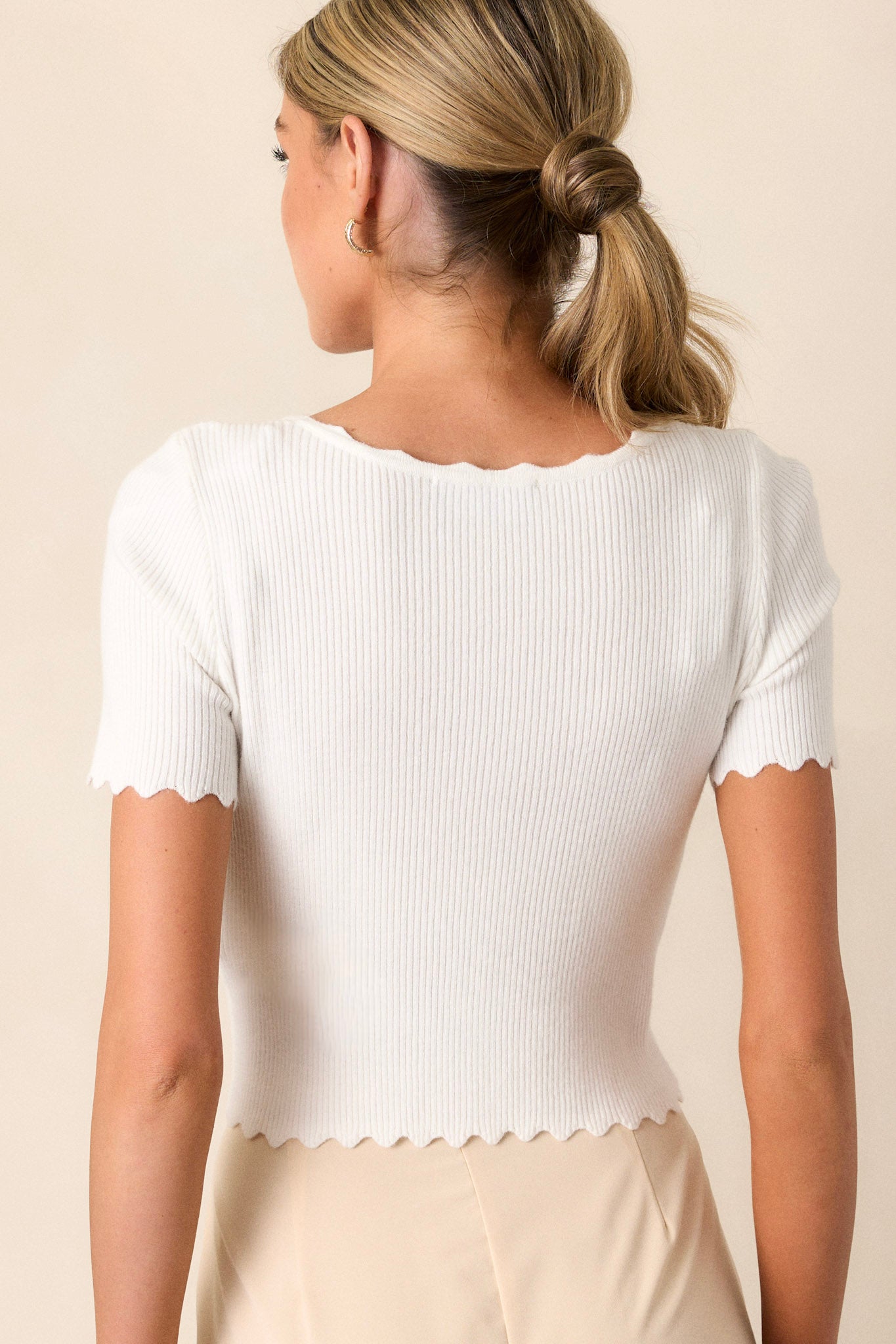 Back of this ivory scallop top that features a round neckline, a scallop trim, a ribbed material, a cropped design, and short sleeves.