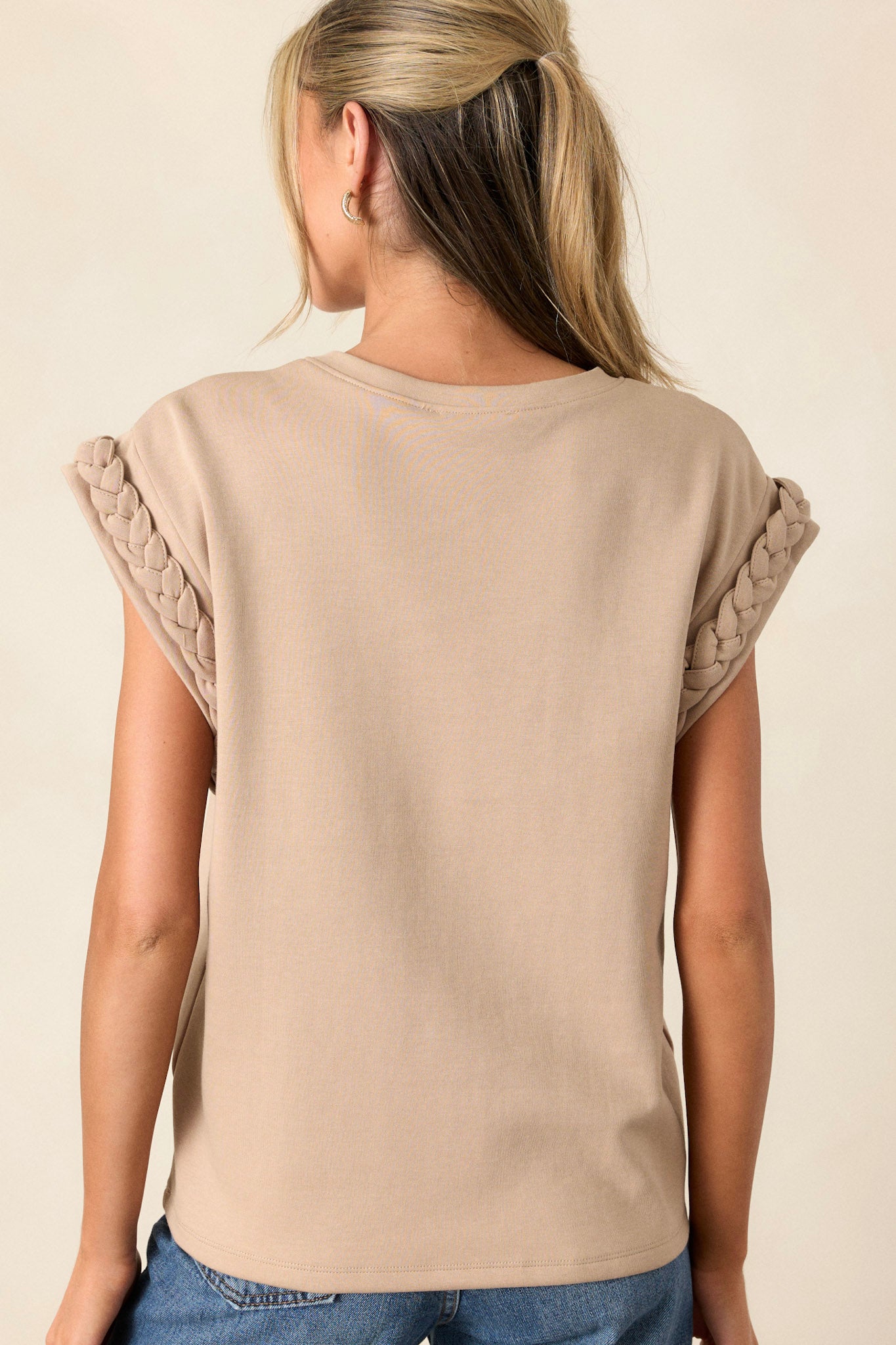 Back view of the taupe top highlighting the simple, clean lines of the high rounded neckline and the cap sleeves with braided trim.