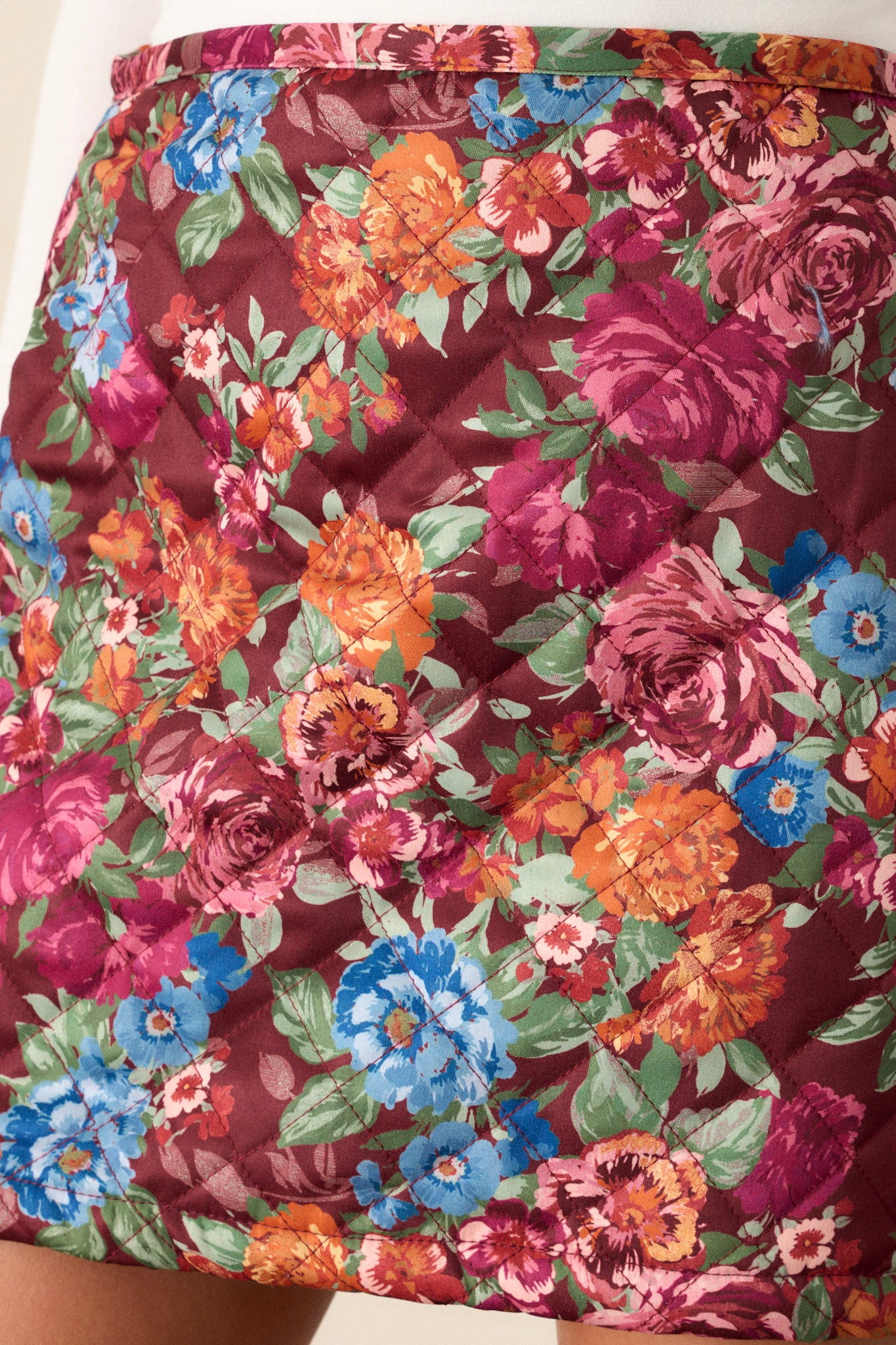 Close-up of the floral print skirt focusing on the zipper closure with a loop button and the quilted puffer design.