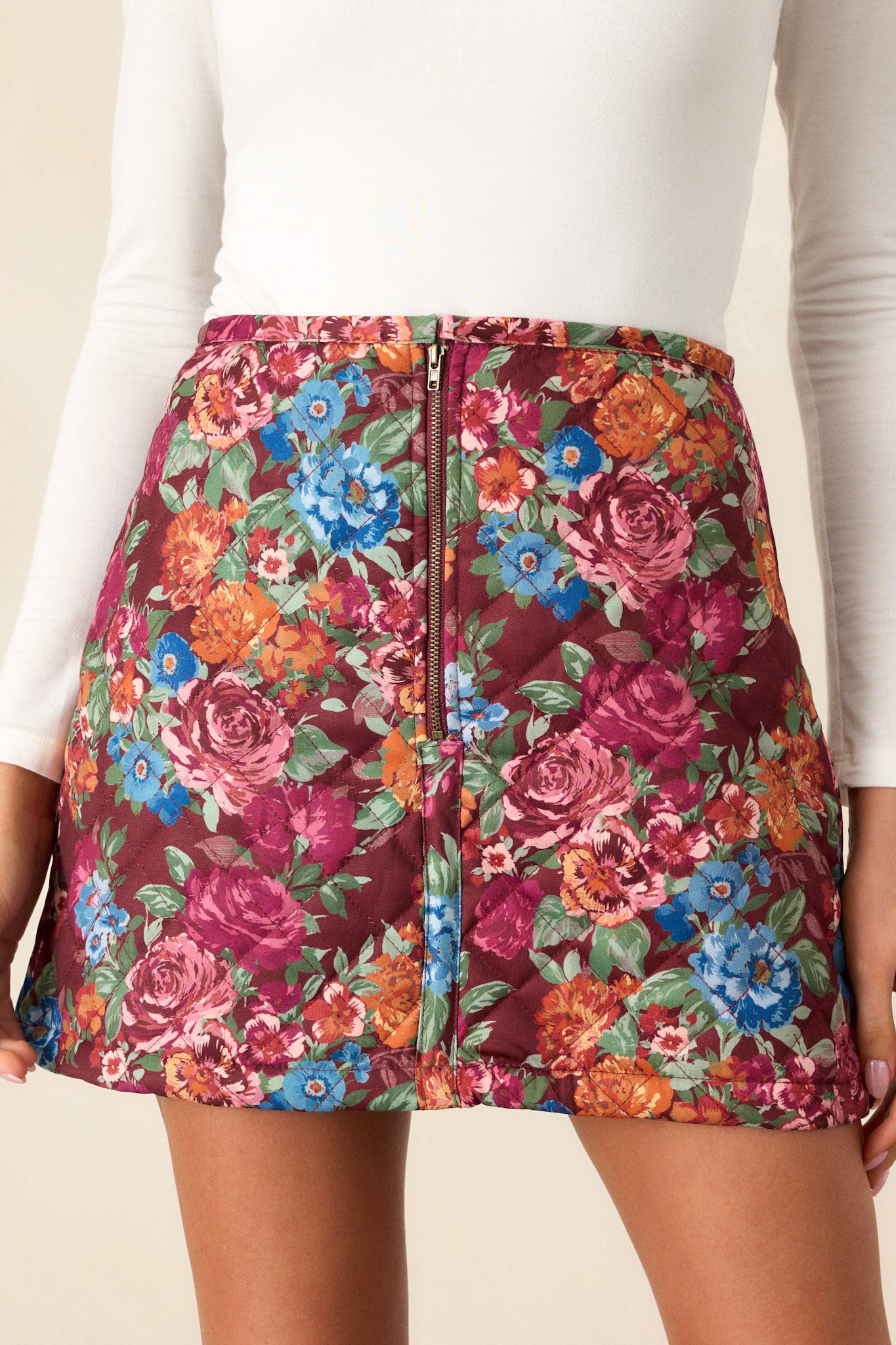 Front view of a floral print skirt featuring a high-waist design, zipper closure with a loop button, and a quilted puffer design.