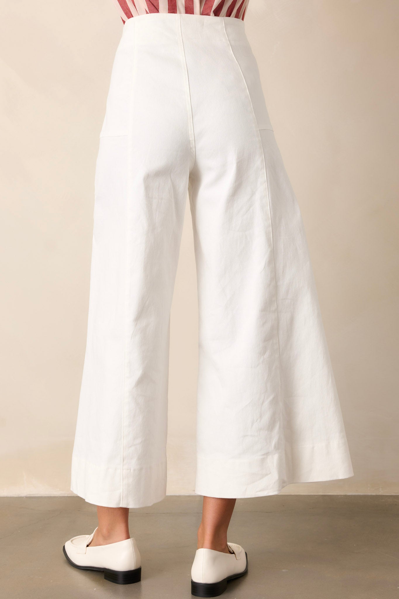 Back view of white pants highlighting the back seams, high waisted design, and wide leg with a cropped length.