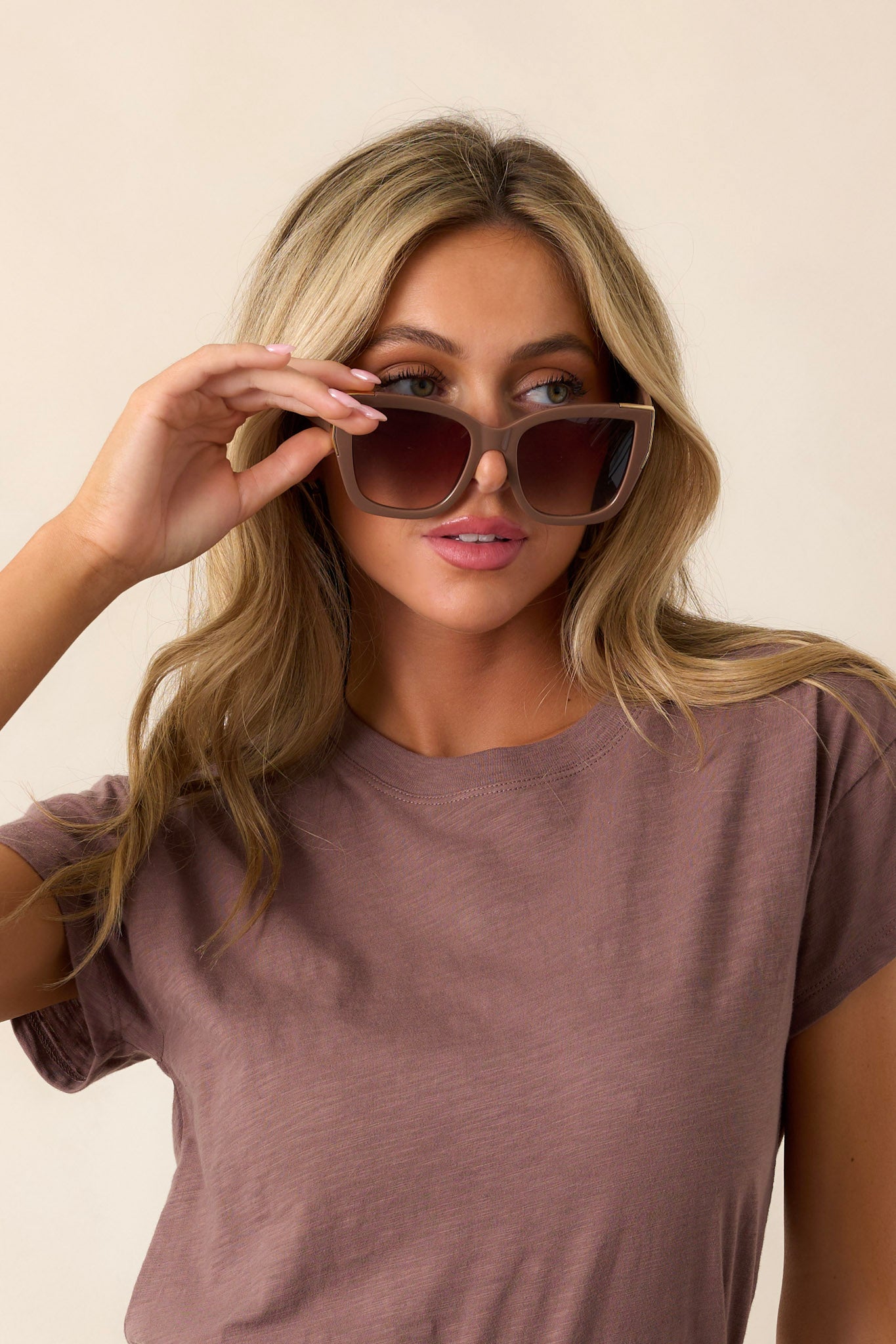 These brown sunglasses feature a cat-eye shape, a color fade lens, and gold detailing around the frame.