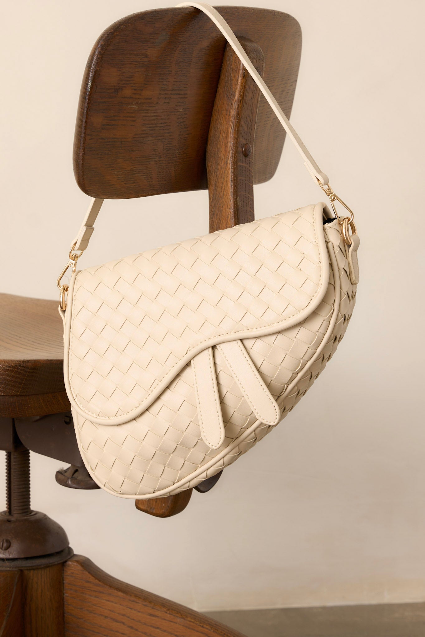 Overhead view of this ivory handbag that features gold hardware, faux leather, a woven design, a magnetic snap closure, a zipper pocket, and an additional strap.