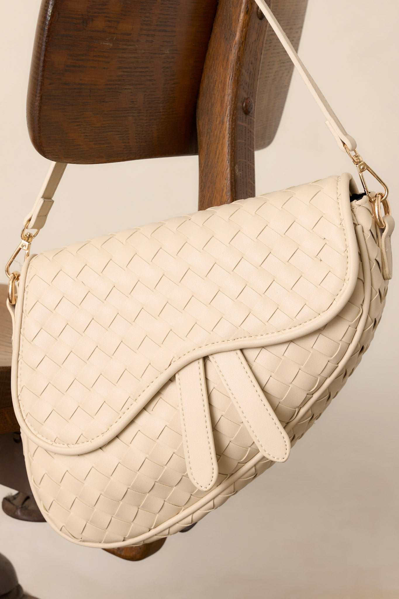 Close-up view of this ivory handbag that features gold hardware, faux leather, a woven design, a magnetic snap closure, a zipper pocket, and an additional strap.