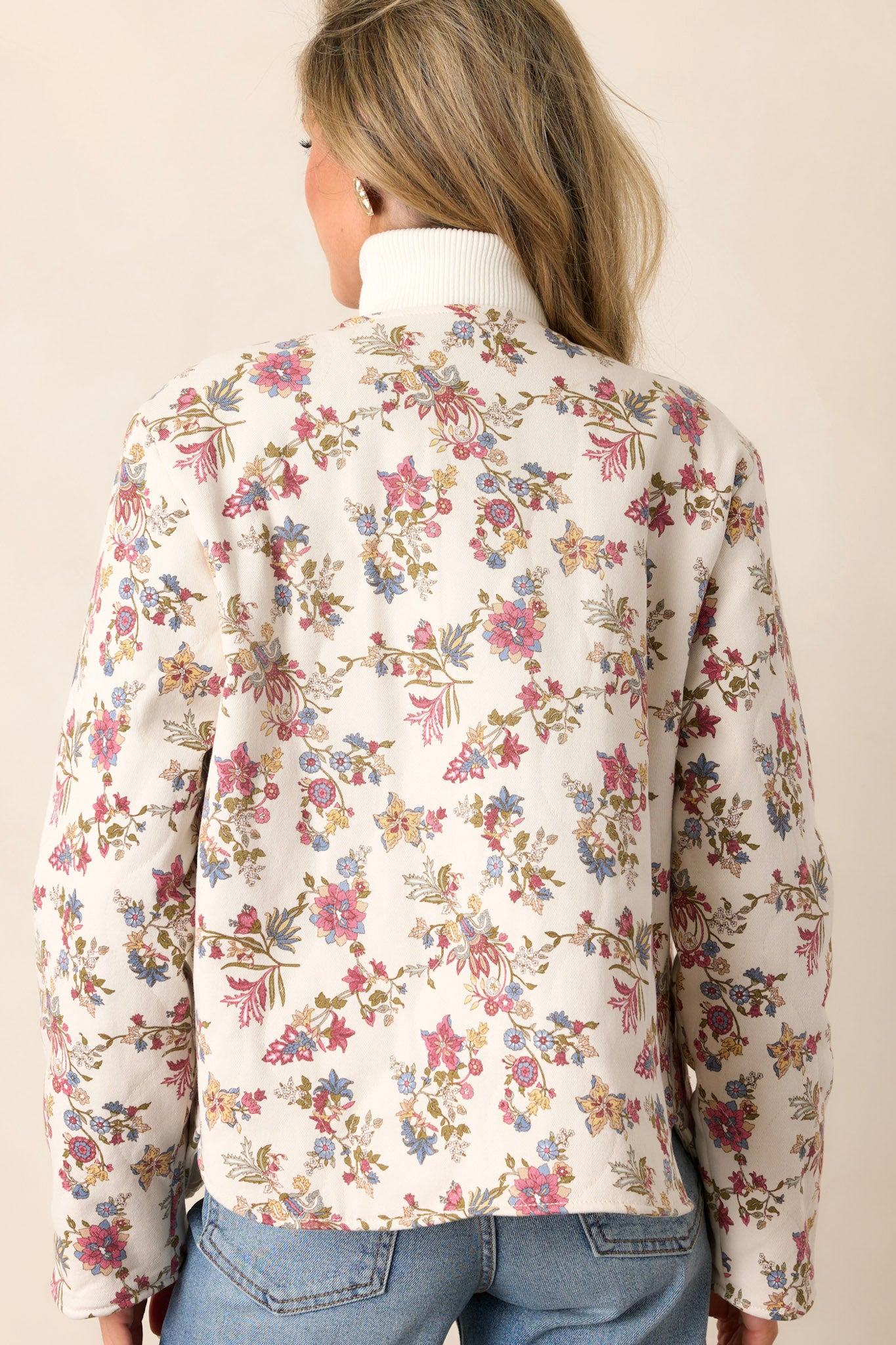 Back view of an ivory floral jacket highlighting the floral denim fabric and the overall structure of the jacket.