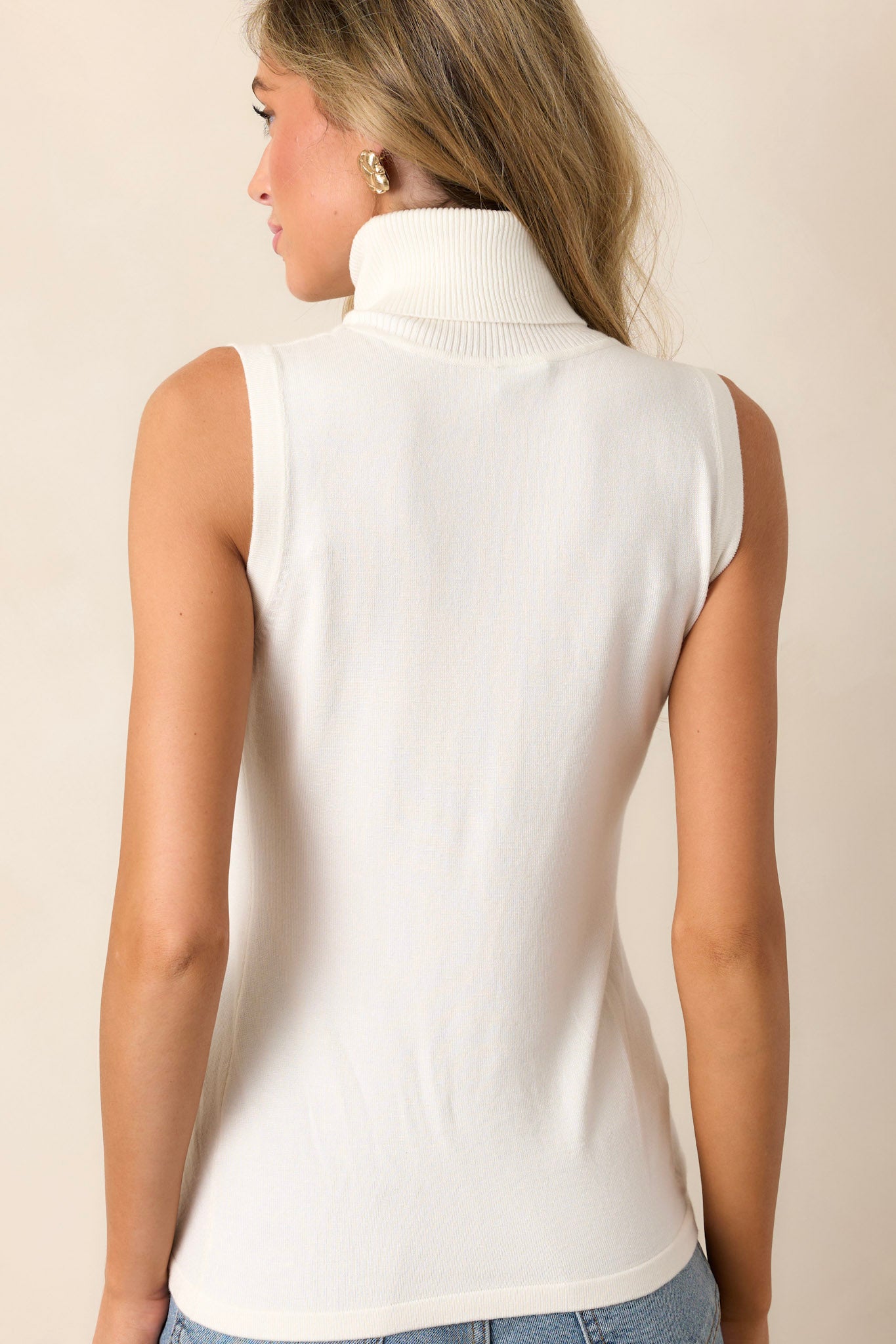 Back view of an ivory ribbed top highlighting the ribbed turtleneck and the overall fit.