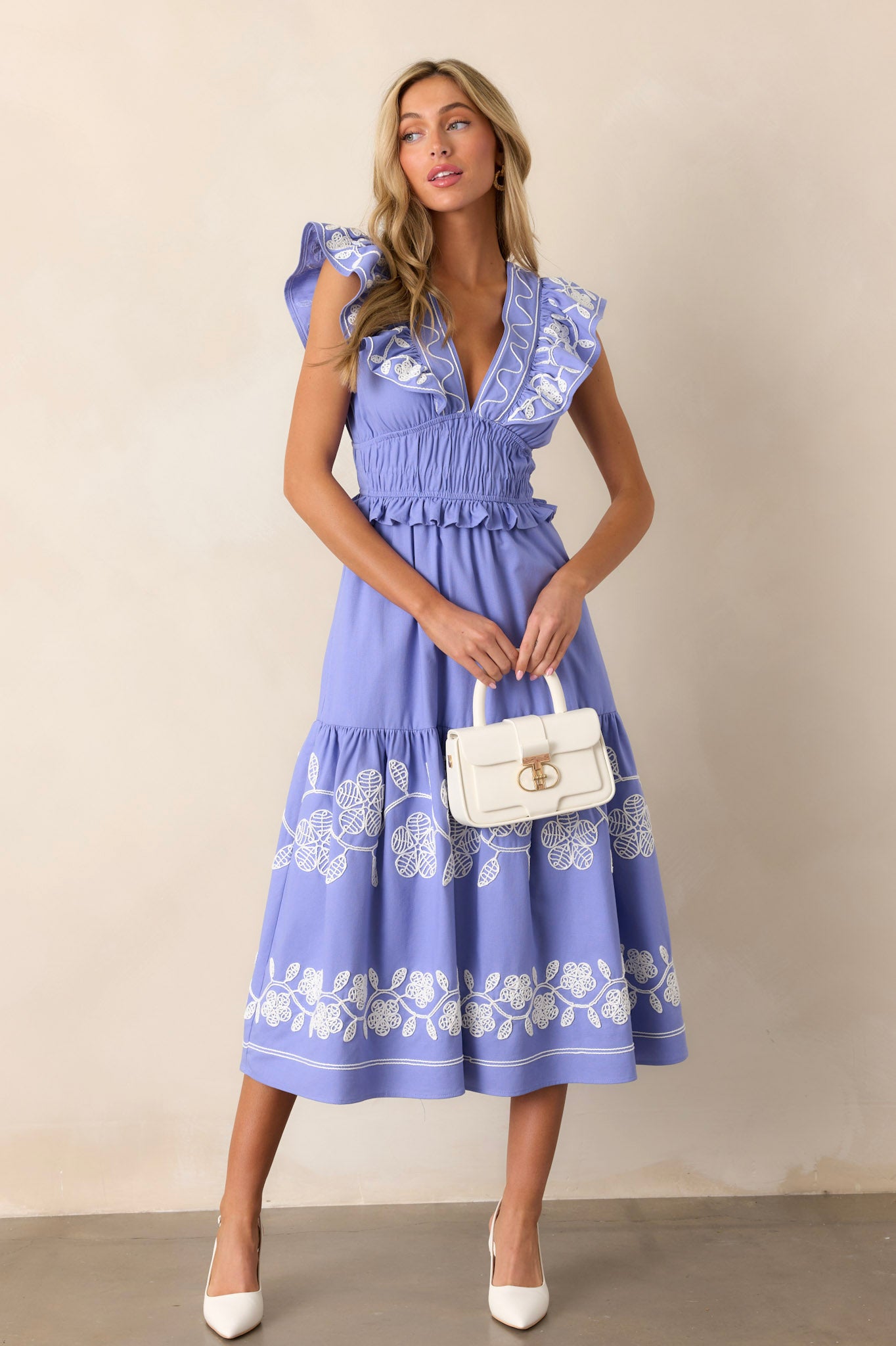 This periwinkle dress features a plunging v-neckline, a smocked waist, functional hip pockets, short flutter sleeves, a discrete back zipper, and embroidered detailing throughout