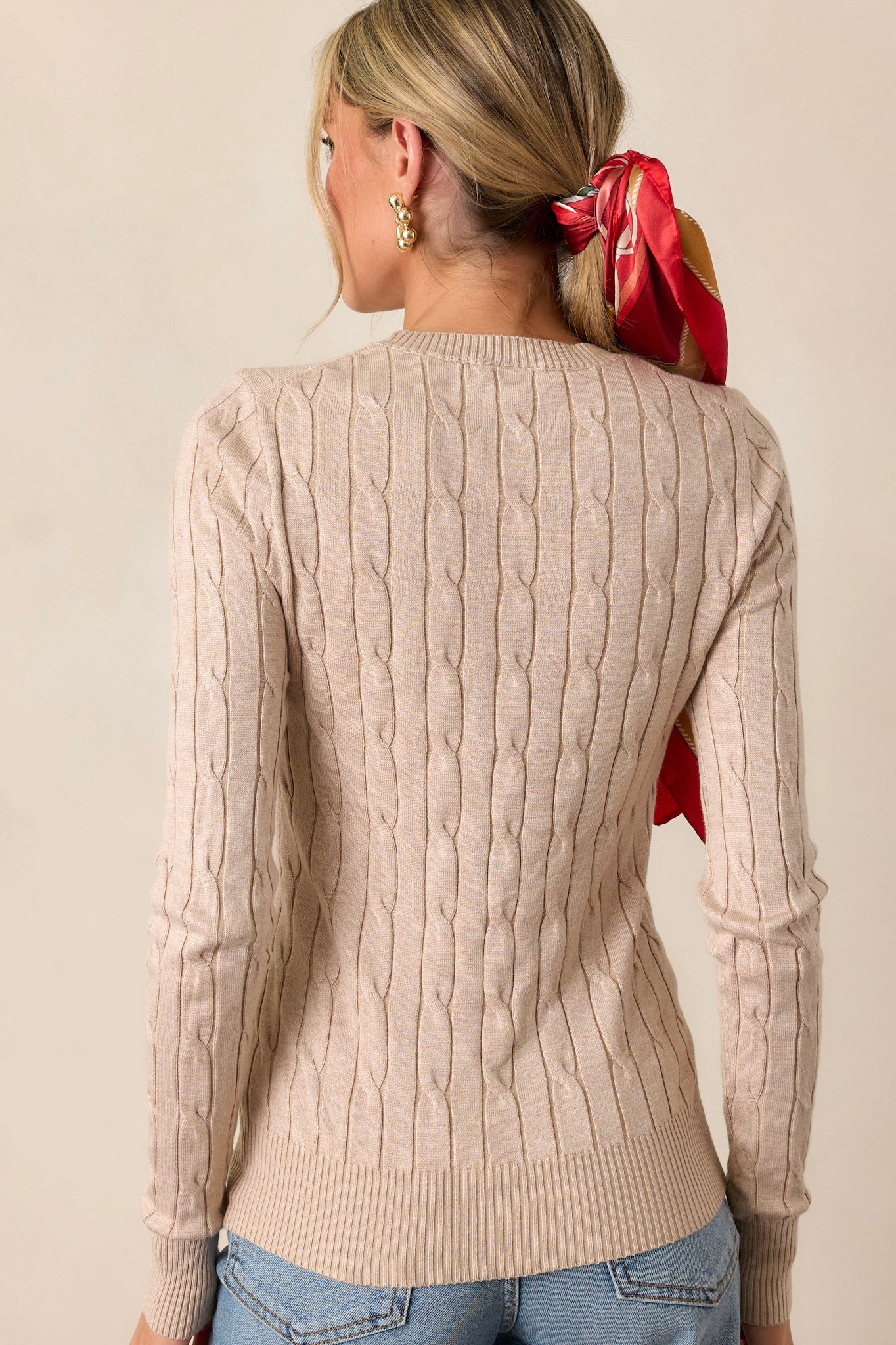 Back view of the beige top highlighting the continuation of the cable knit pattern and the smooth finish of the fabric, with a clear view of the ribbed wrists and neckline