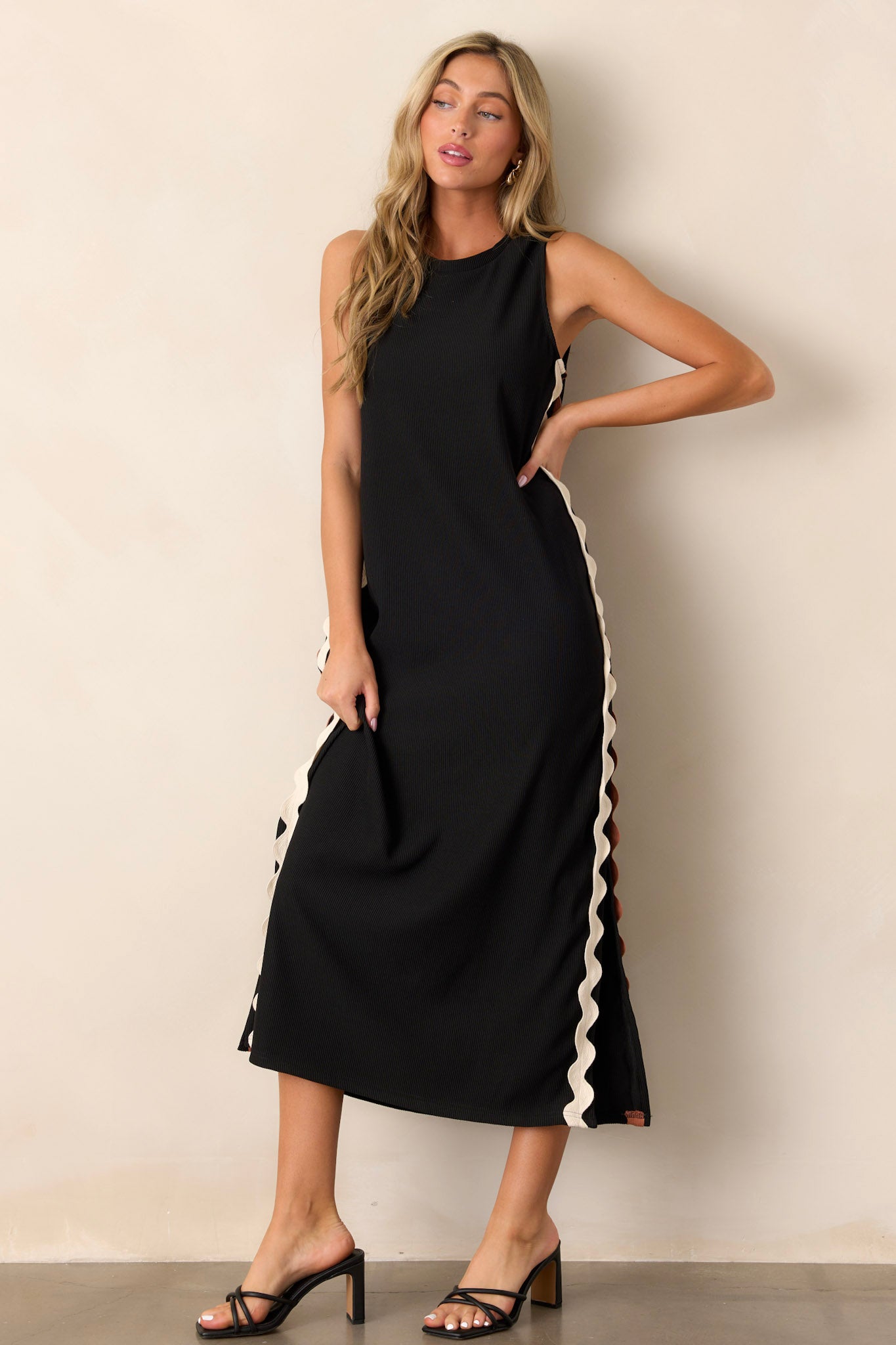 This black midi dress features a crew neckline, a ribbed material, two-toned ricrac side detailing, side slits, and a sleeveless design.