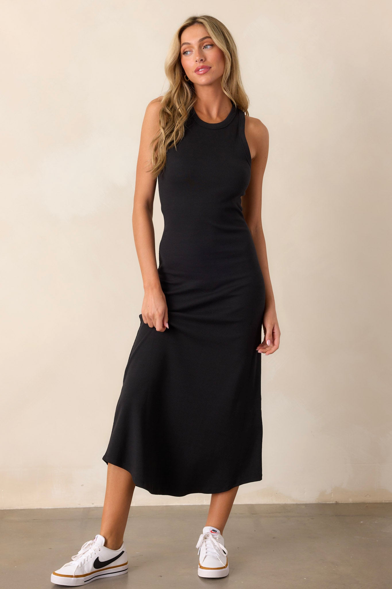 Front view of a black dress featuring a ribbed fabric, a scoop hem, and a bodycon design.