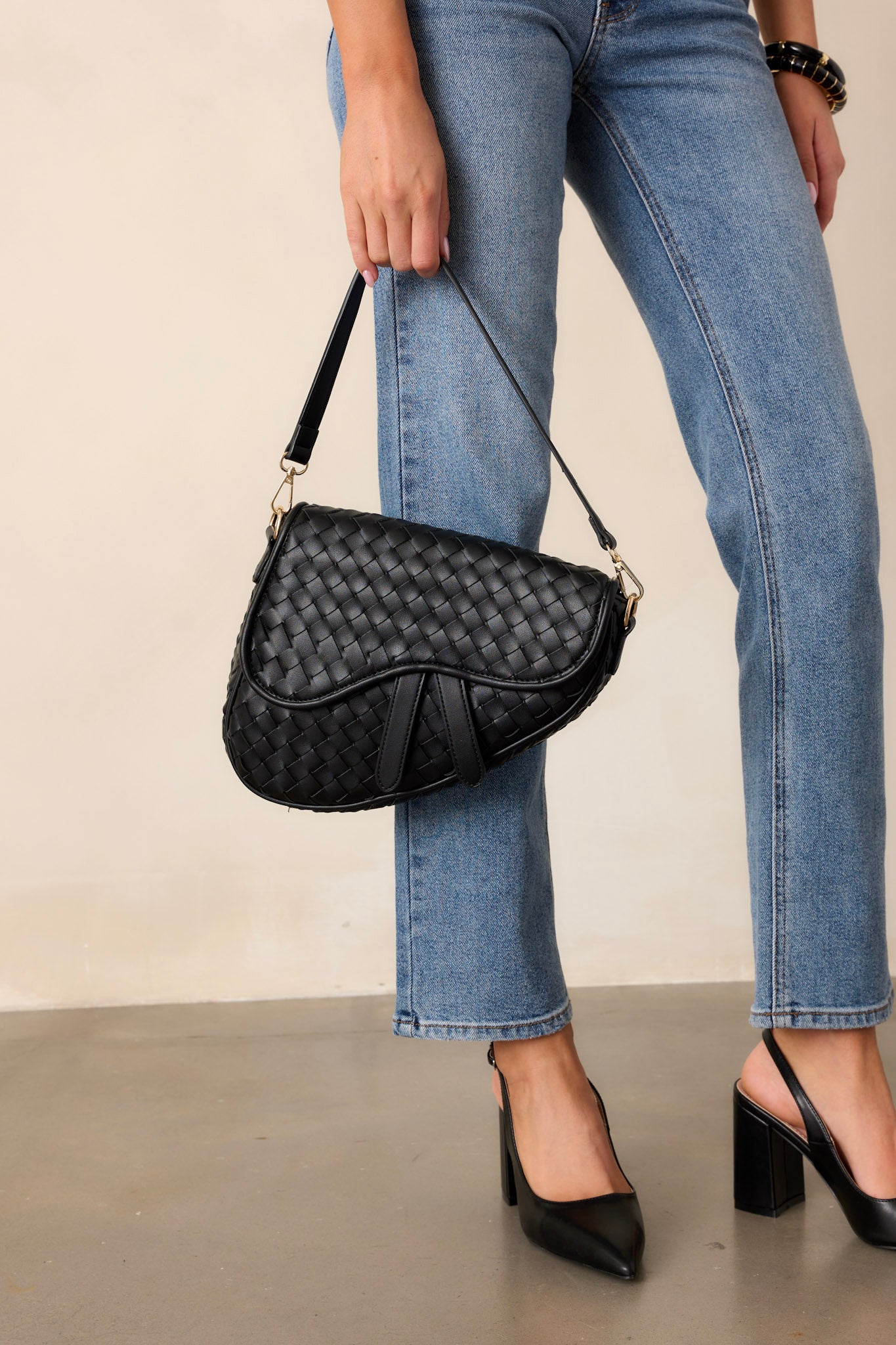 This black handbag features gold hardware, faux leather, a woven design, a magnetic snap closure, a zipper pocket, and an additional strap.