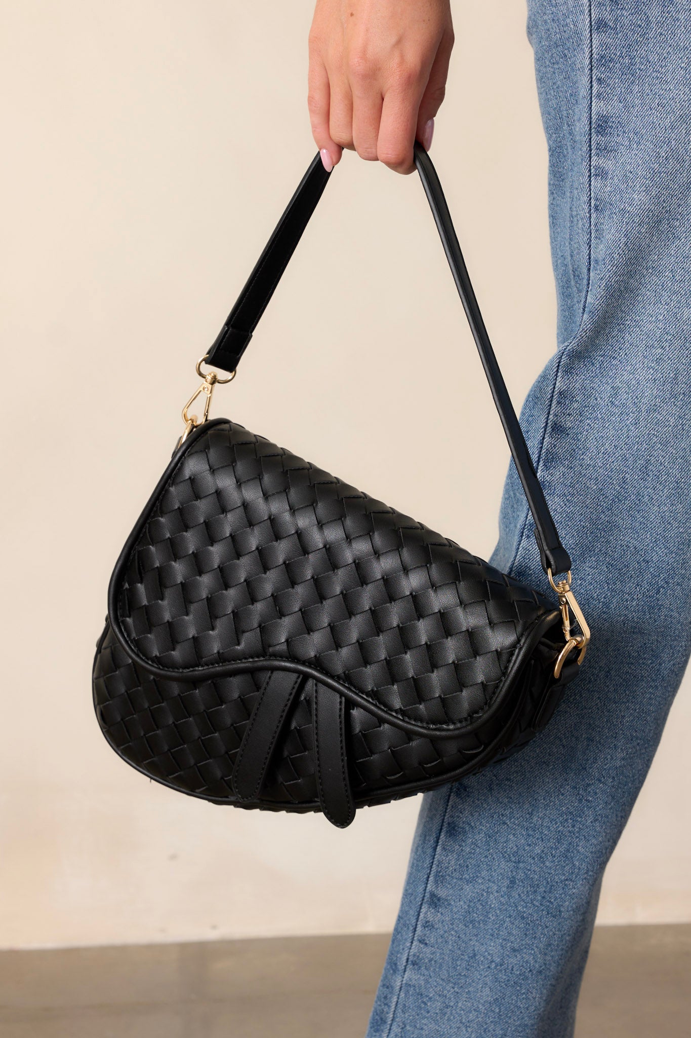 Close-up of this black handbag that features gold hardware, faux leather, a woven design, a magnetic snap closure, a zipper pocket, and an additional strap.