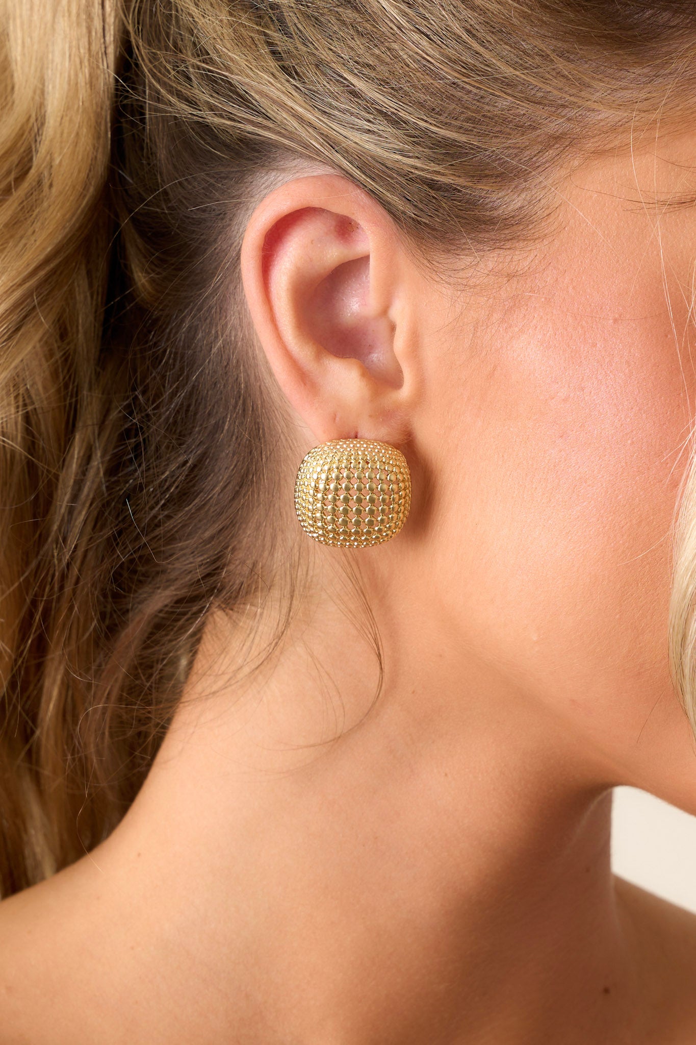 Close-up of these gold earrings that feature a square shape, a textured design, and secure post hole backings.