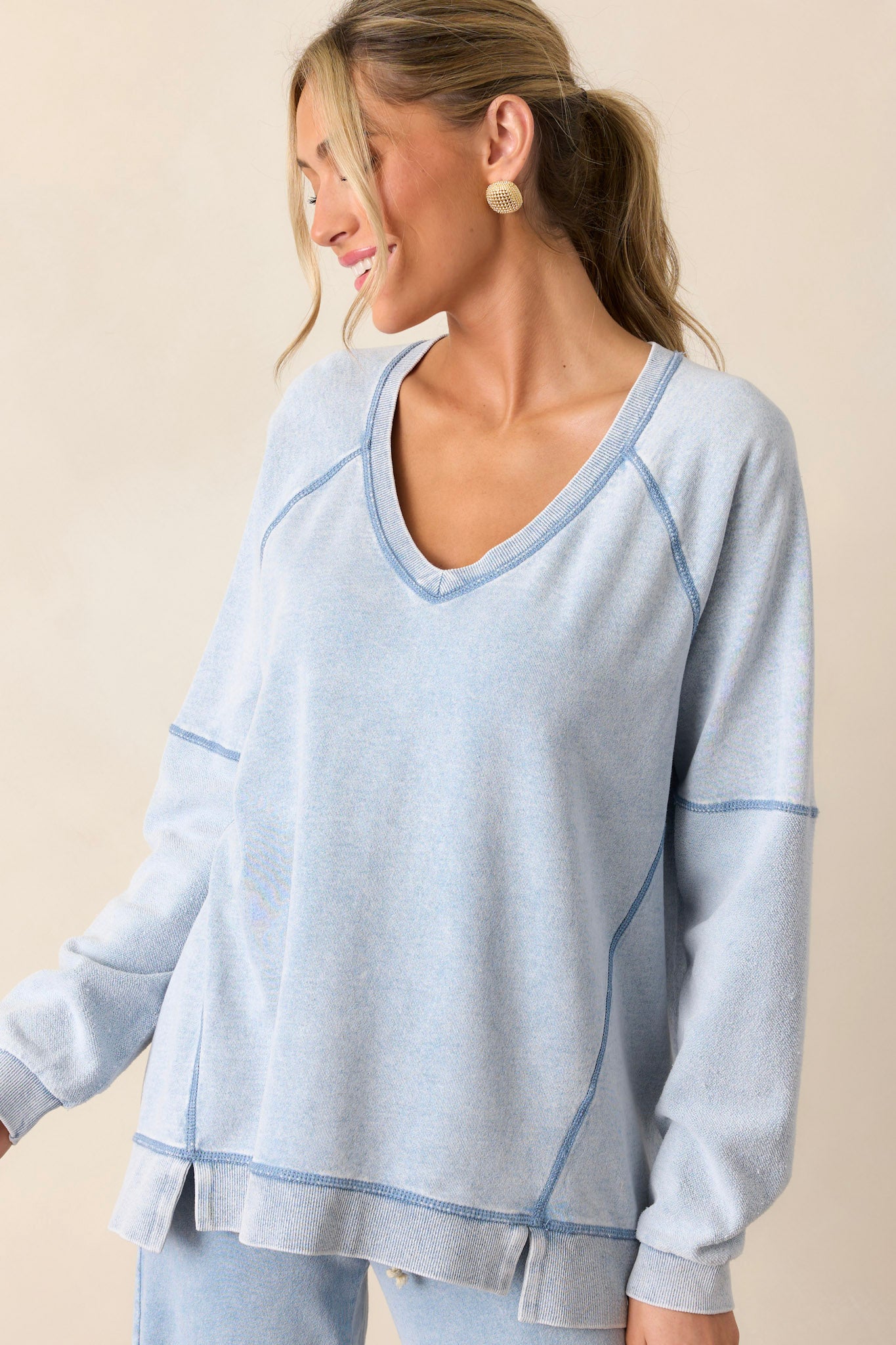 Front angled view of the indigo sweatshirt featuring a v-neckline, soft knit texture, side slits in the hemline, and long sleeves