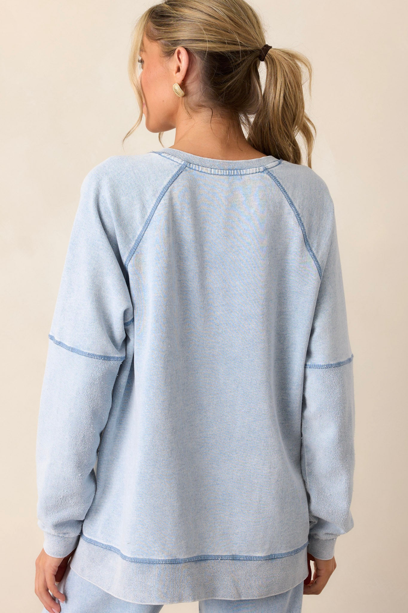 Back view of the indigo sweatshirt highlighting the soft knit texture, side slits in the hemline, and the long sleeves from behind.