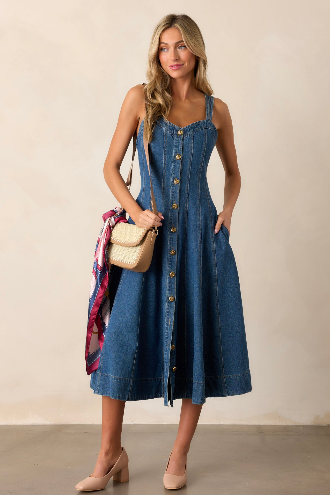 Front view of this dark wash midi dress made with high-quality denim, featuring a sweetheart neckline, thin straps, functional pockets, functional buttons down the length of the dress, and vertical seam detailing.