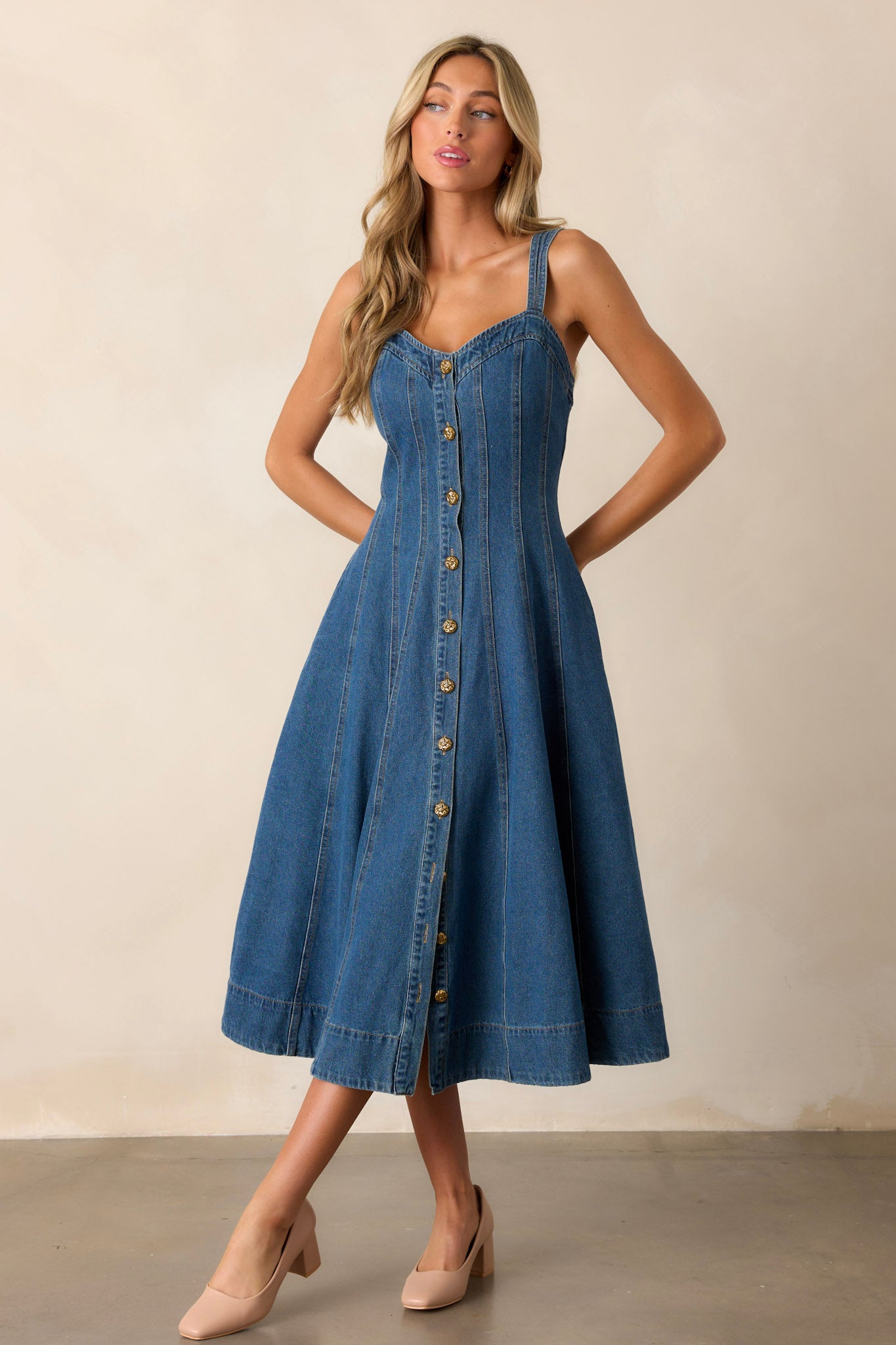 Full body view of this dark wash midi dress made with high-quality denim, featuring a sweetheart neckline, thin straps, functional pockets, functional buttons down the length of the dress, and vertical seam detailing.