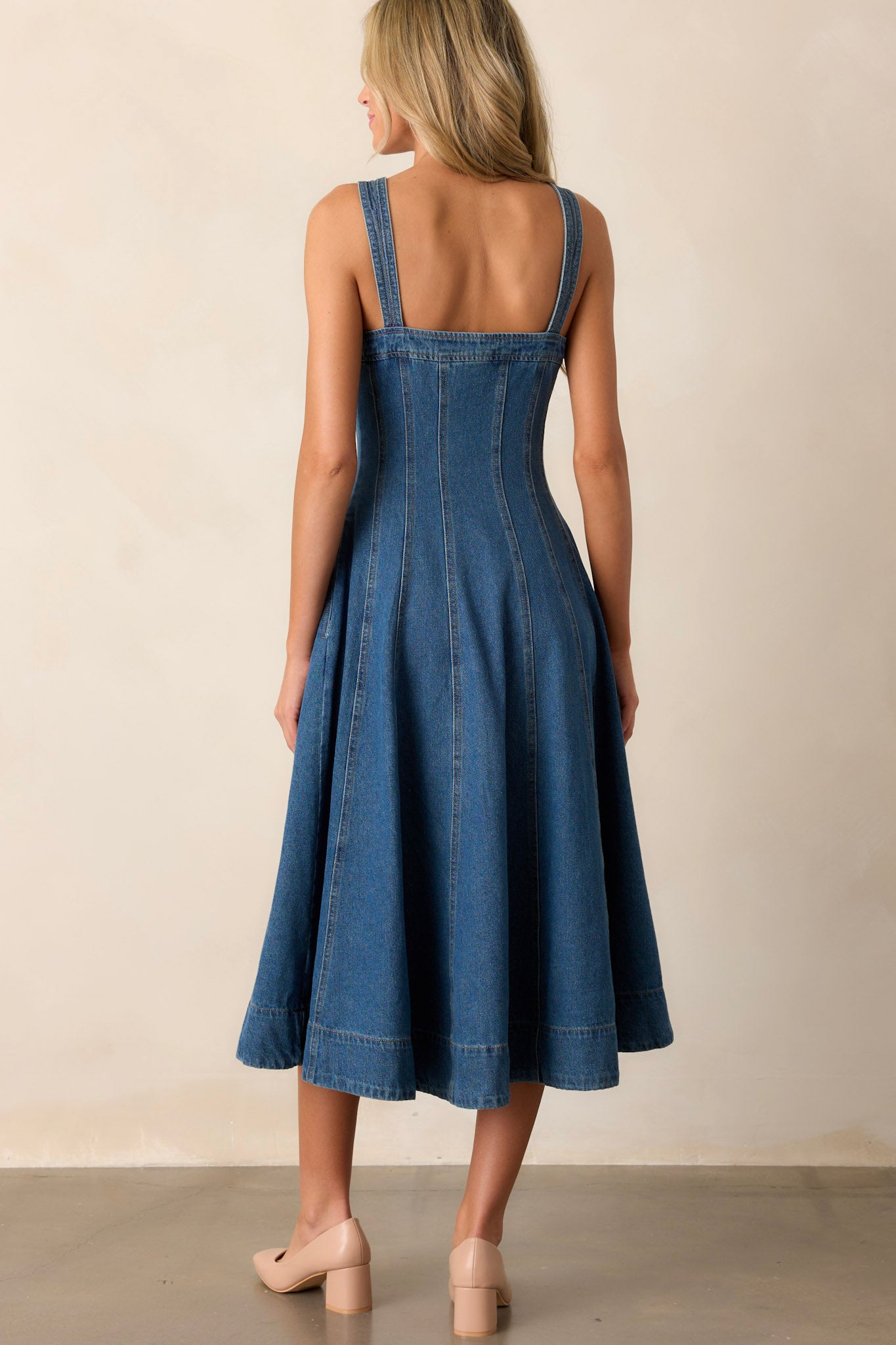 Back view of this dark wash midi dress made with high-quality denim, featuring a sweetheart neckline, thin straps, functional pockets, functional buttons down the length of the dress, and vertical seam detailing.