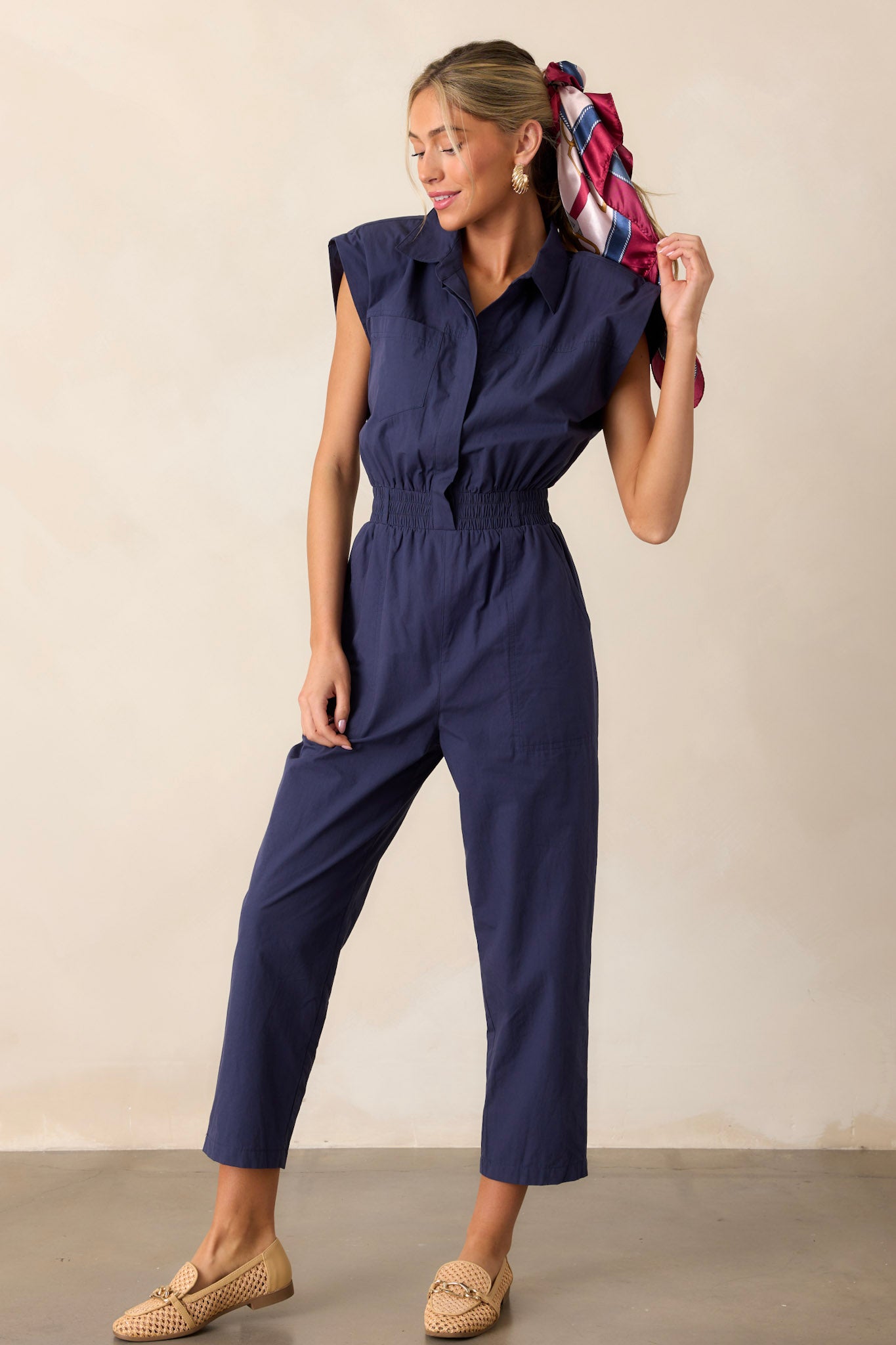 Front angled view of a jumpsuit featuring a popped collar, two side pockets, and a stretchy soft waistband