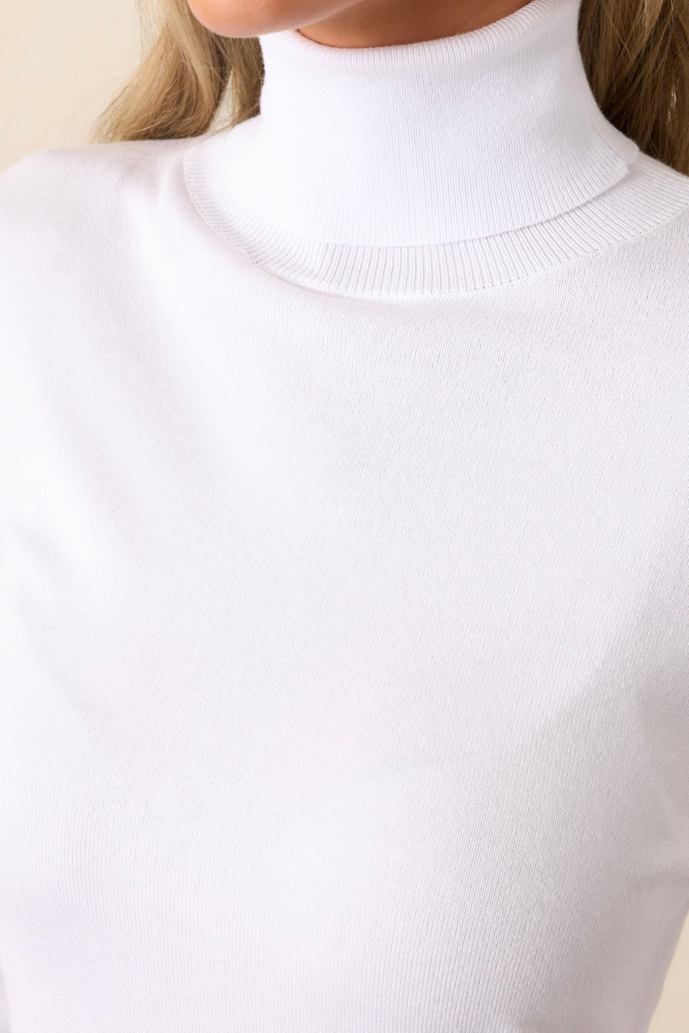 Close-up detail of the white sweater showcasing the turtle neckline, ribbed cuffs, and the soft fabric texture.