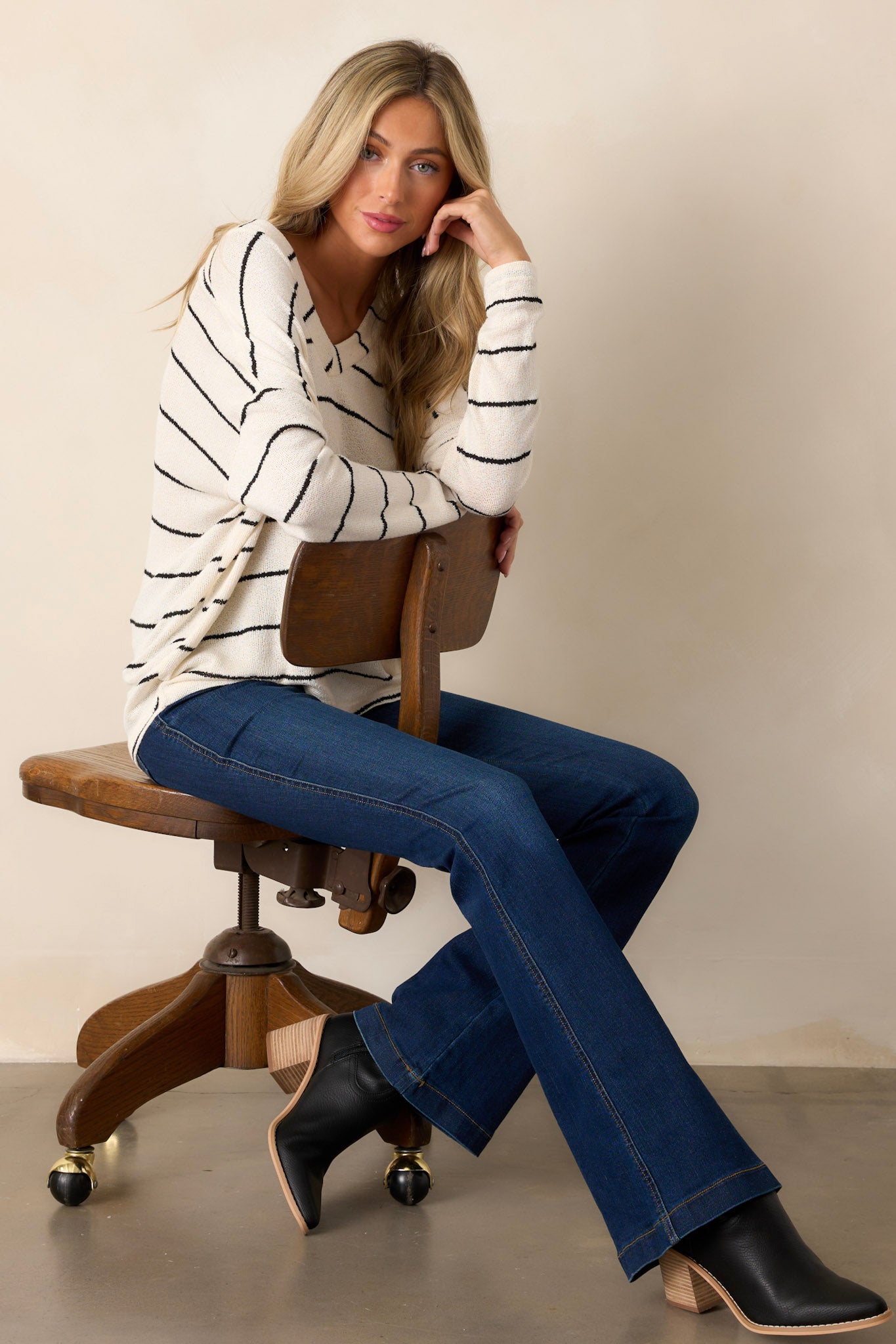 Seated Full length view of a sweater featuring a v-neckline, horizontal stripe pattern, lightweight breathable knit fabric, and long sleeves